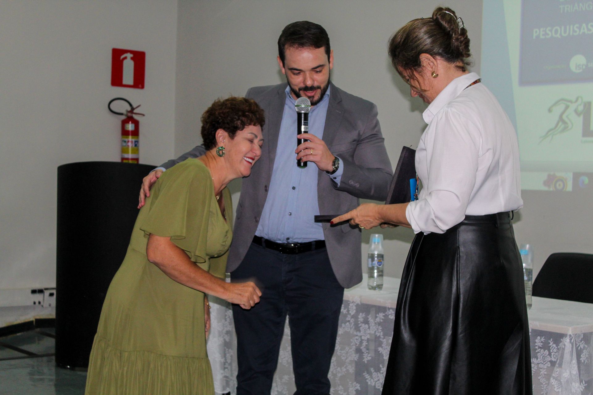 Um homem e duas mulheres estão de pé, um ao lado do outro, em uma sala.