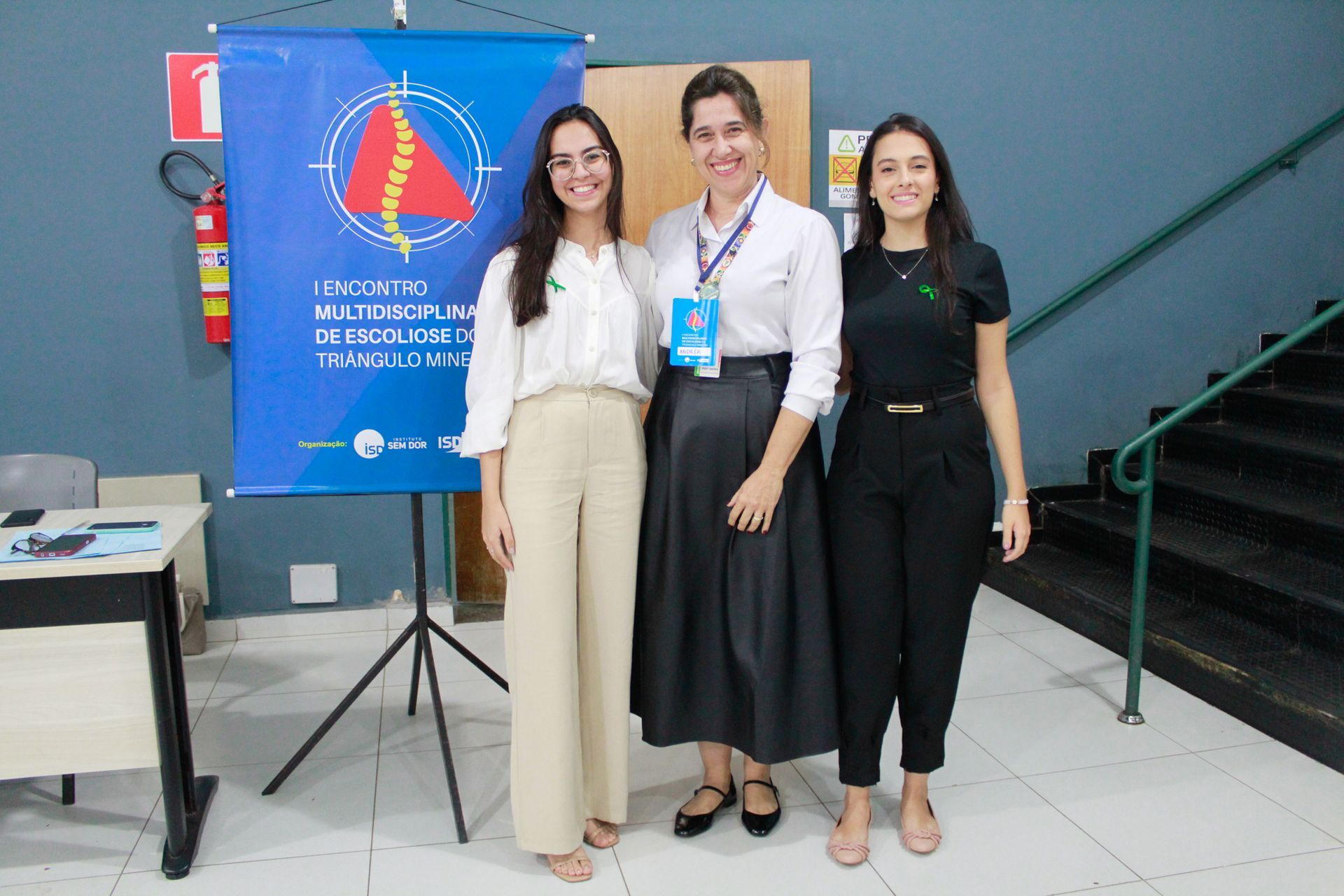 Três mulheres estão posando para uma foto em frente a uma faixa azul.