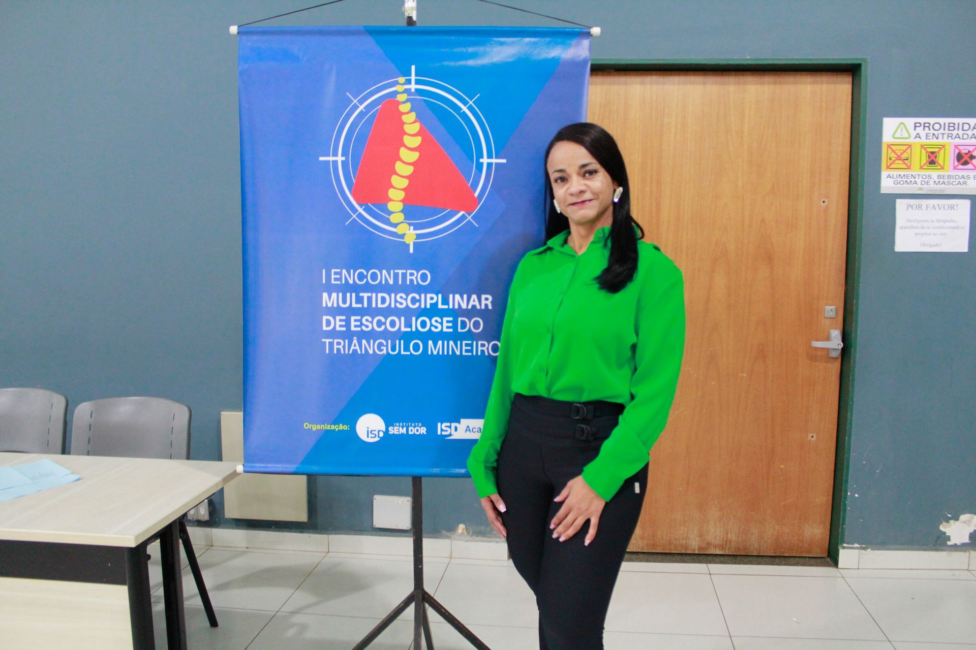 Uma mulher de camisa verde está parada em frente a uma faixa azul.