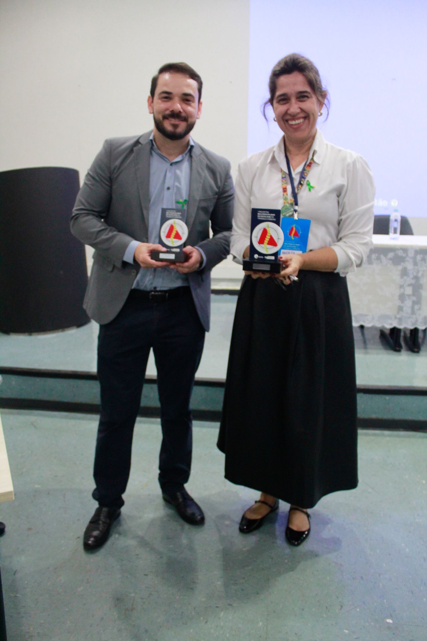 Um homem e uma mulher estão de pé, um ao lado do outro, segurando troféus.