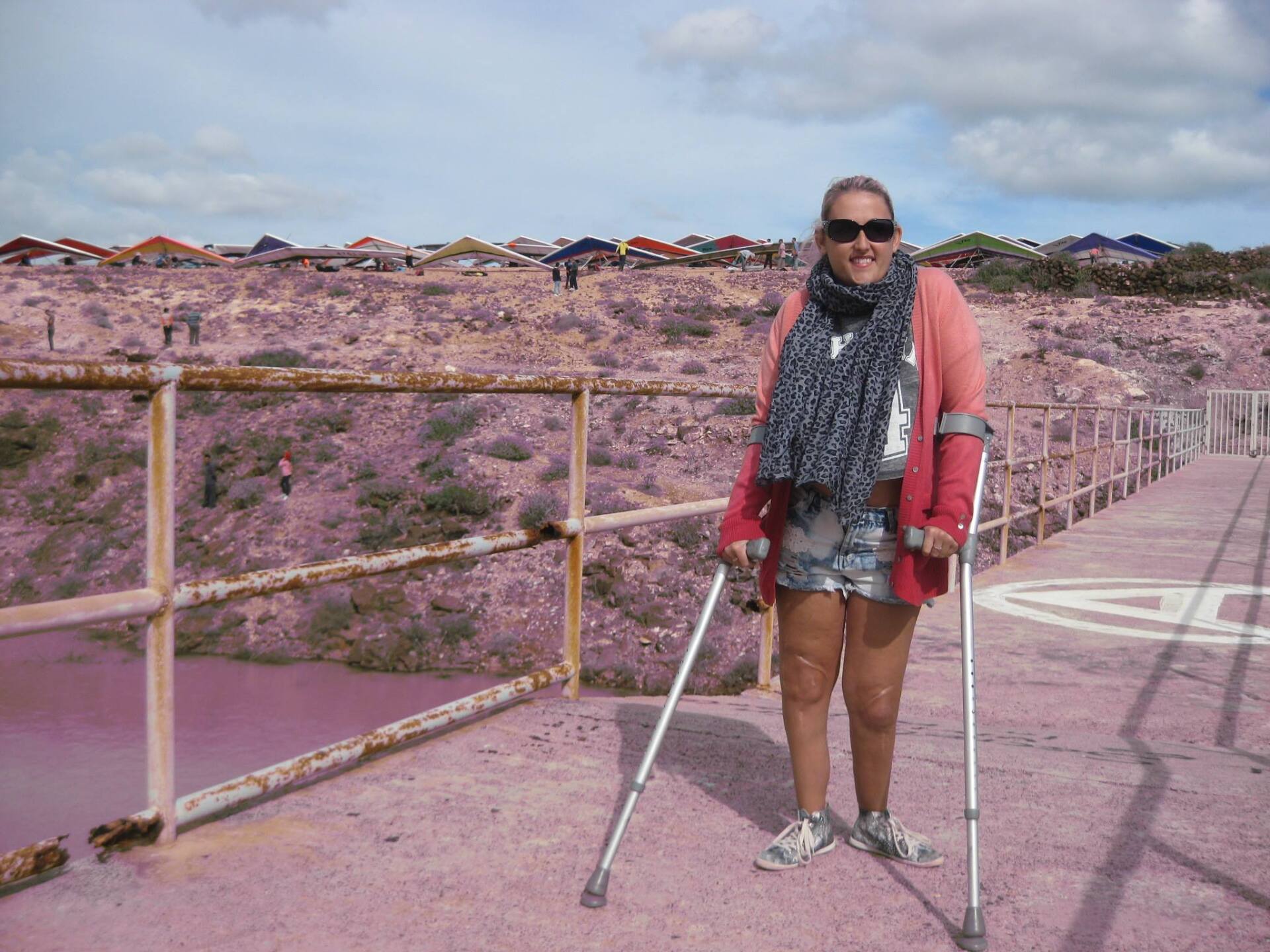 A woman with crutches is standing in front of a fence