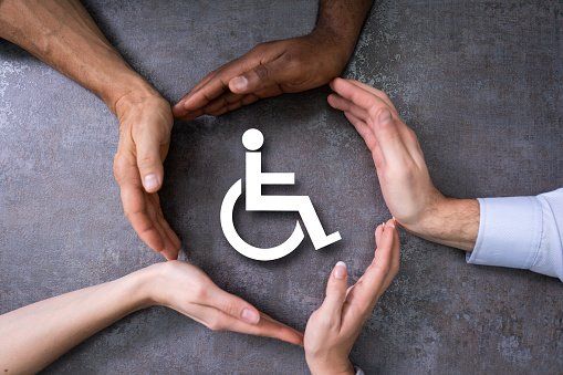 A group of people are making a circle with their hands around a wheelchair.