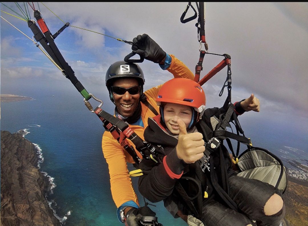 Two people are flying a parachute and one is giving a thumbs up