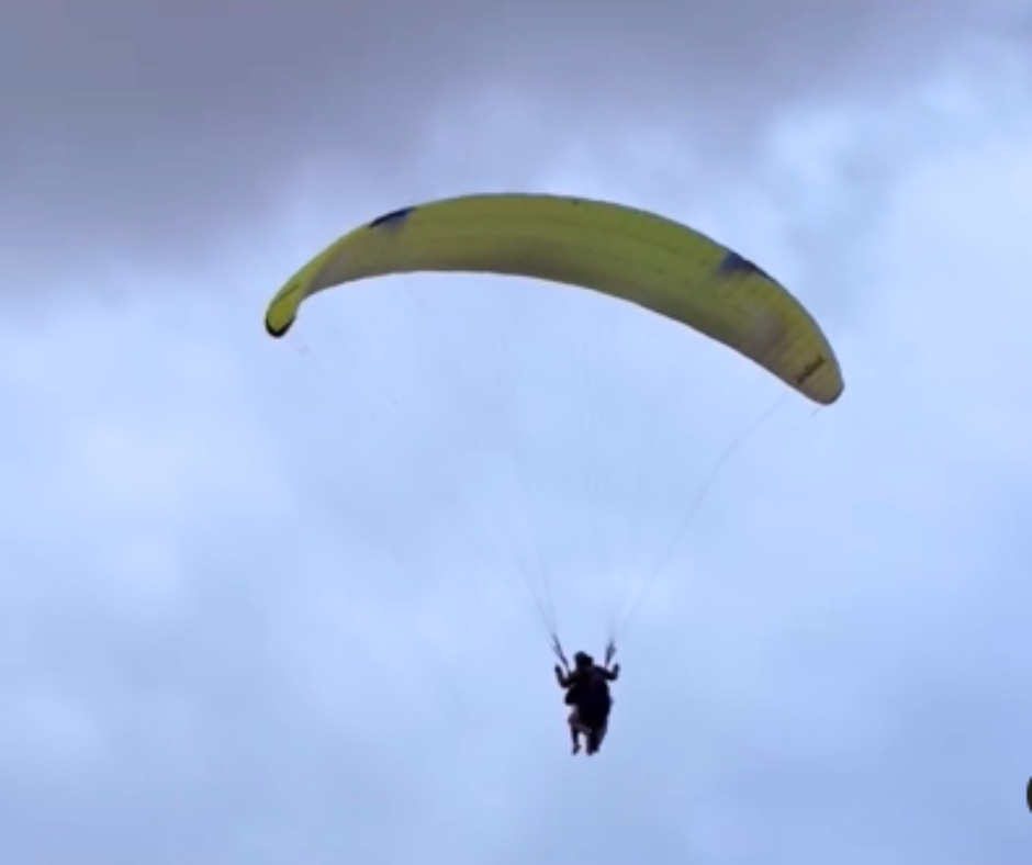 A person is parasailing in the sky with a yellow parachute