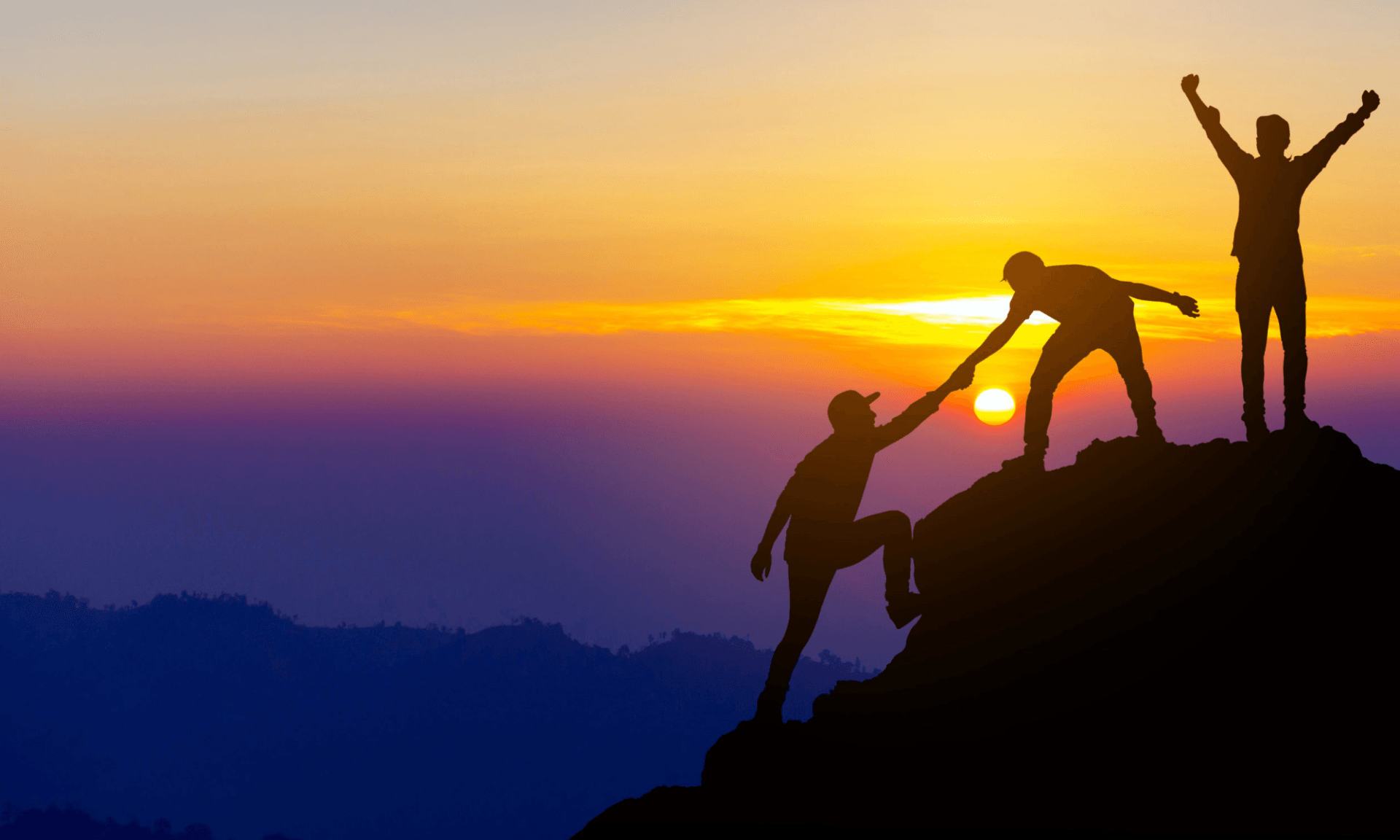 A man is helping another man climb a mountain at sunset.