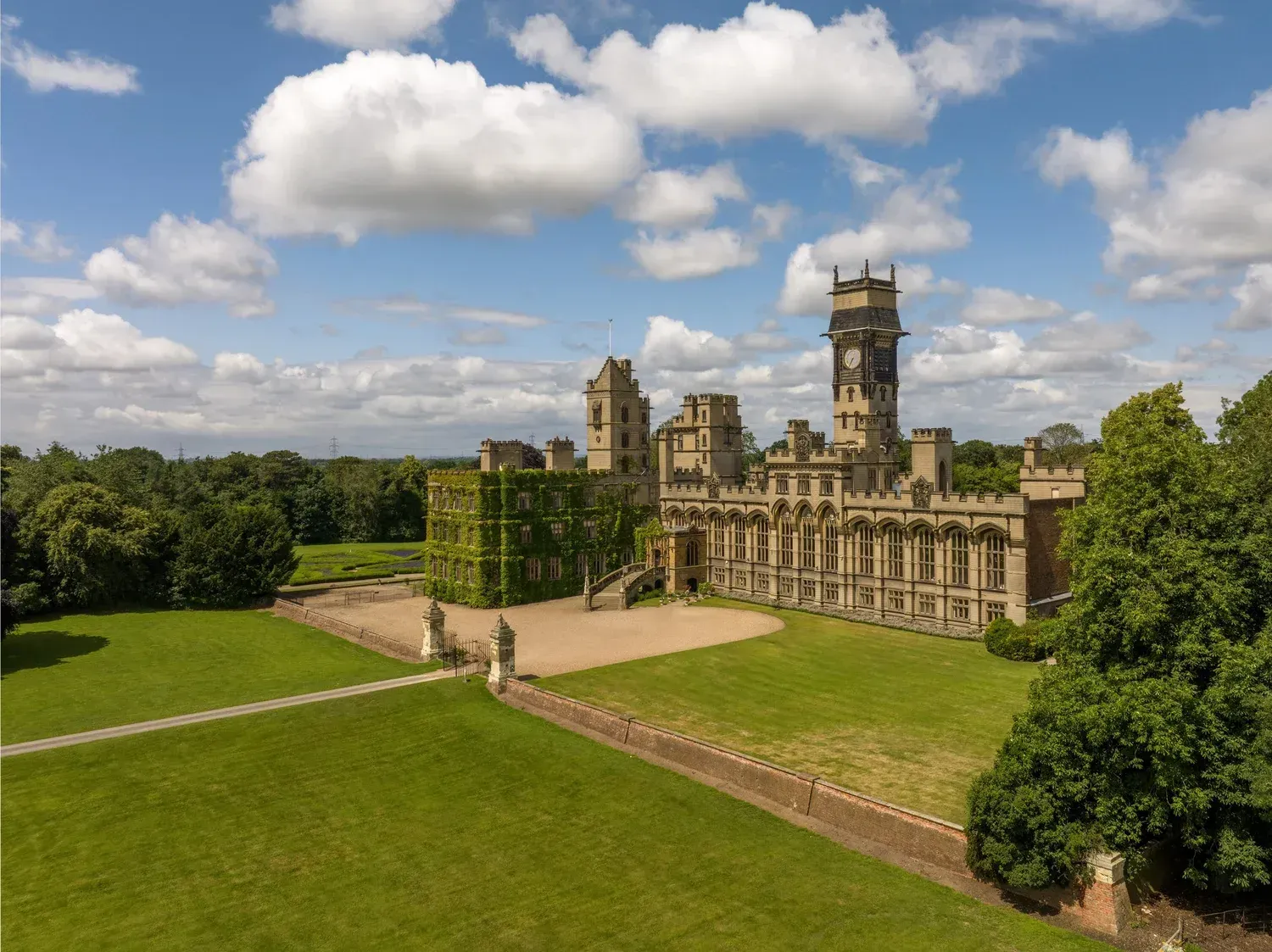 Historic stone castle with towers beside a large green lawn under a cloudy sky