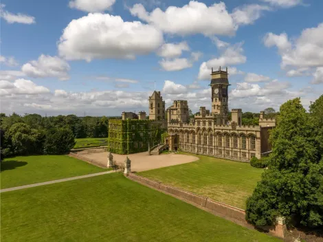 Historic stone castle with towers beside a large green lawn under a cloudy sky