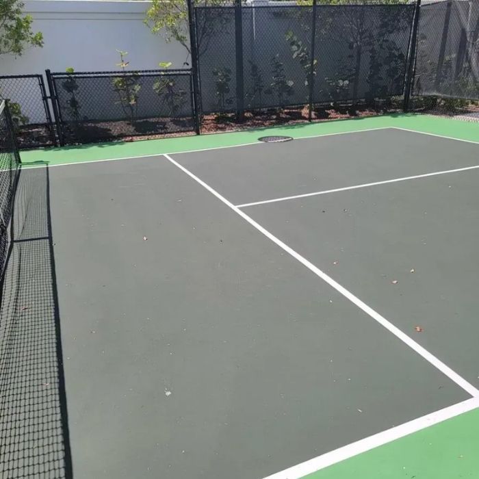 Empty outdoor tennis court with green and gray surface and black chain-link fencing.