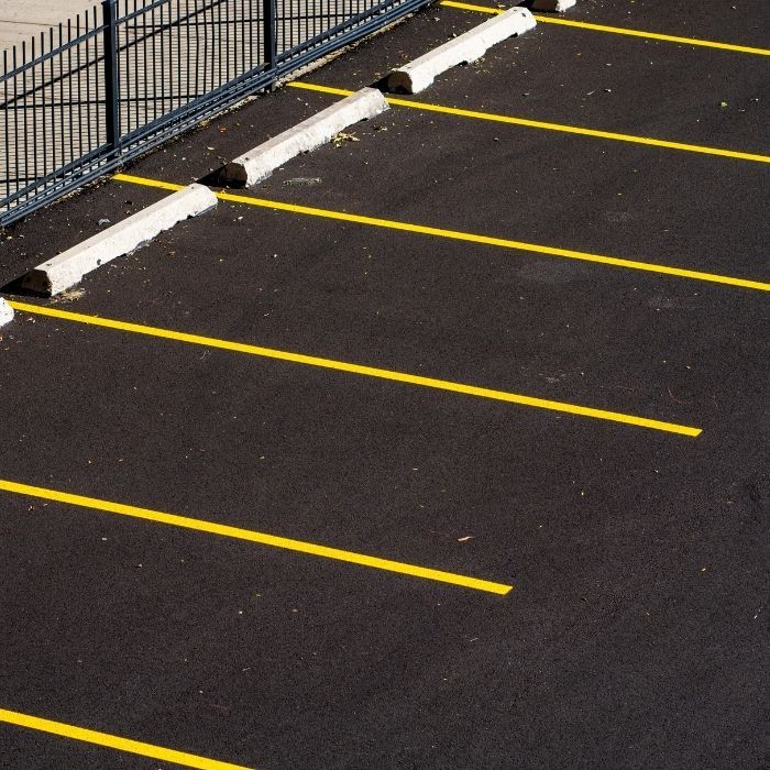 Empty parking lot with yellow lines and white wheel stops along a fence