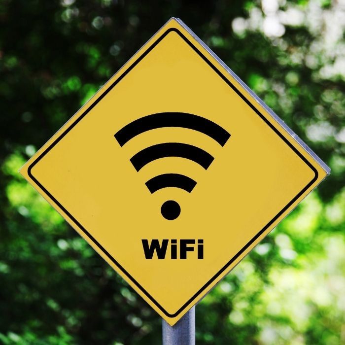 Yellow Wi-Fi warning sign with black wireless symbol and text, outdoors against blurred greenery