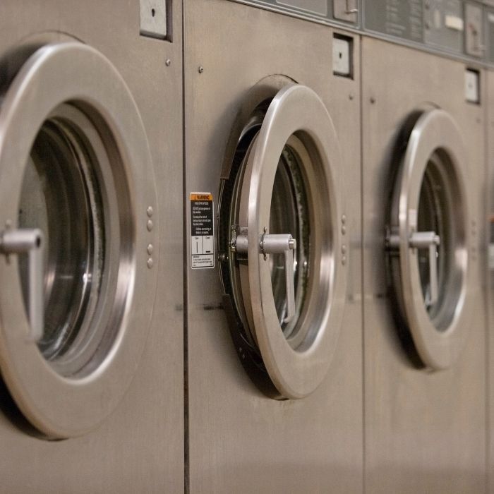 Row of stainless steel front-loading washing machines in a laundromat