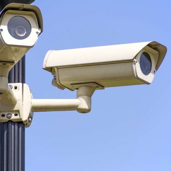 Two white security cameras mounted on a pole against a clear blue sky