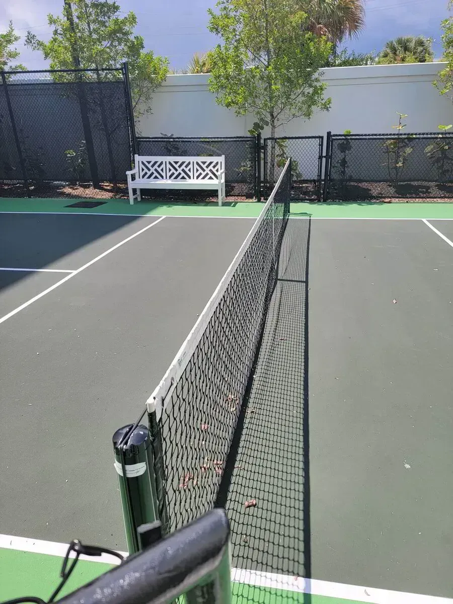 Tennis court with a net centered between two gray playing surfaces and a white bench in the background