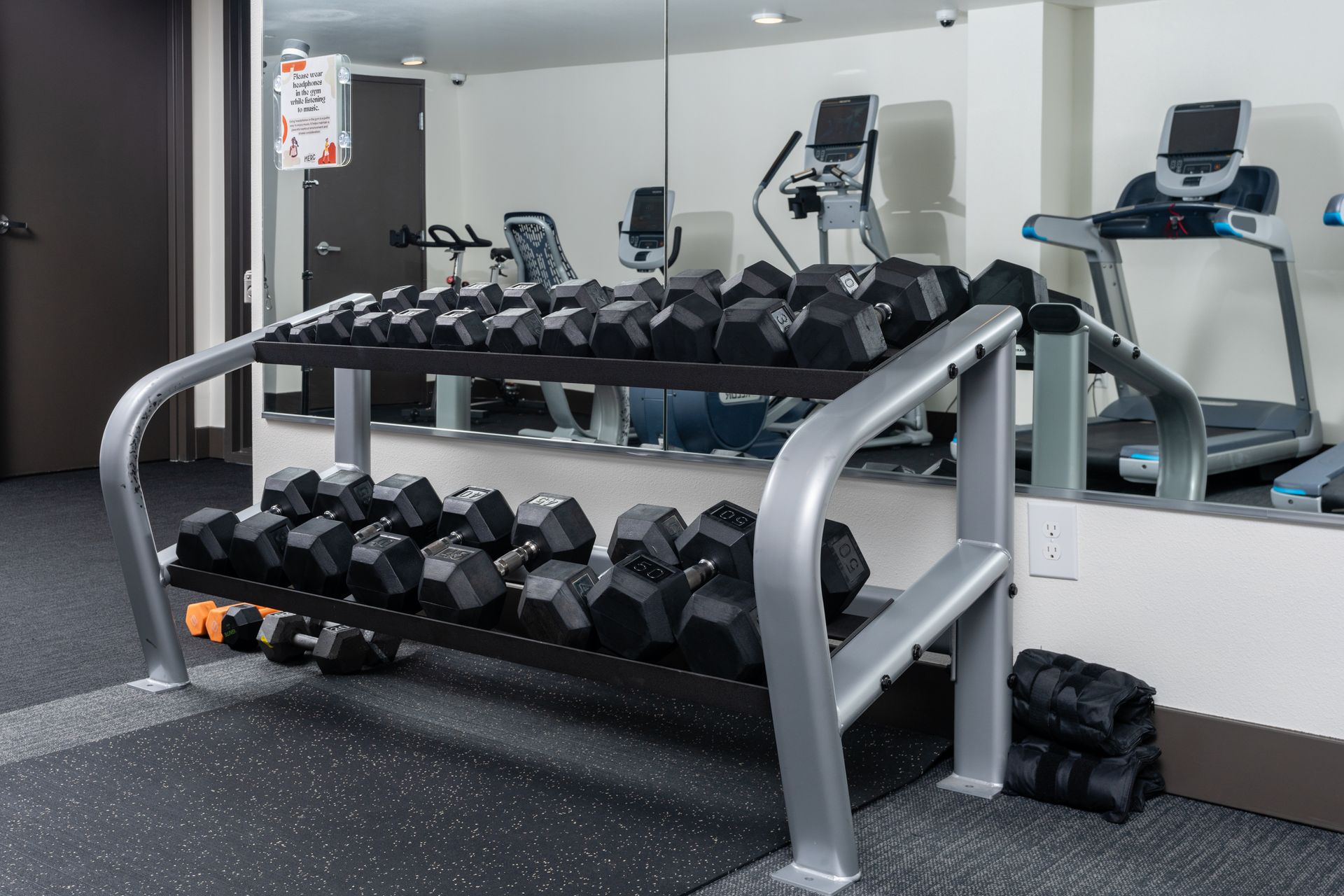A gym with dumbbells and a treadmill in front of a mirror.