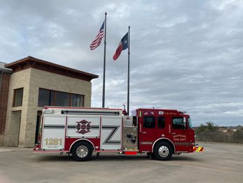 A rMaypearl fire truck is parked in front of a fire station.