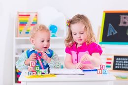 A boy and a girl are sitting at a table playing with blocks.