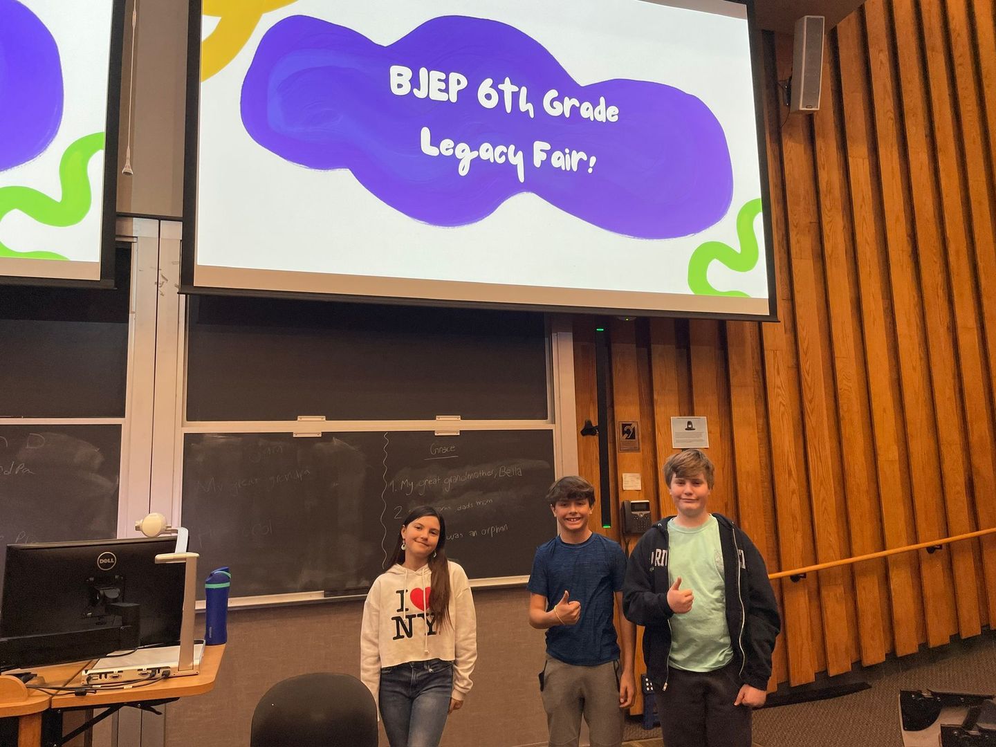 A group of people standing in front of a large screen that says 6th grade legacy fair