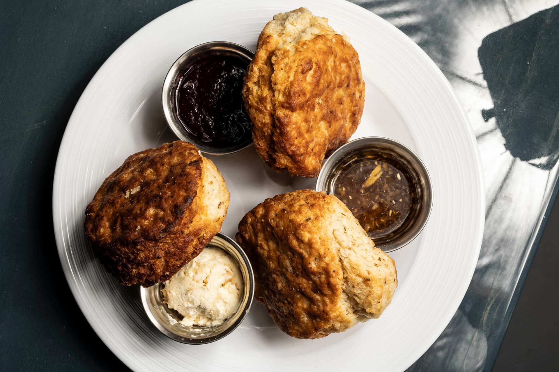 A white plate topped with biscuits , jam , butter and dipping sauce.