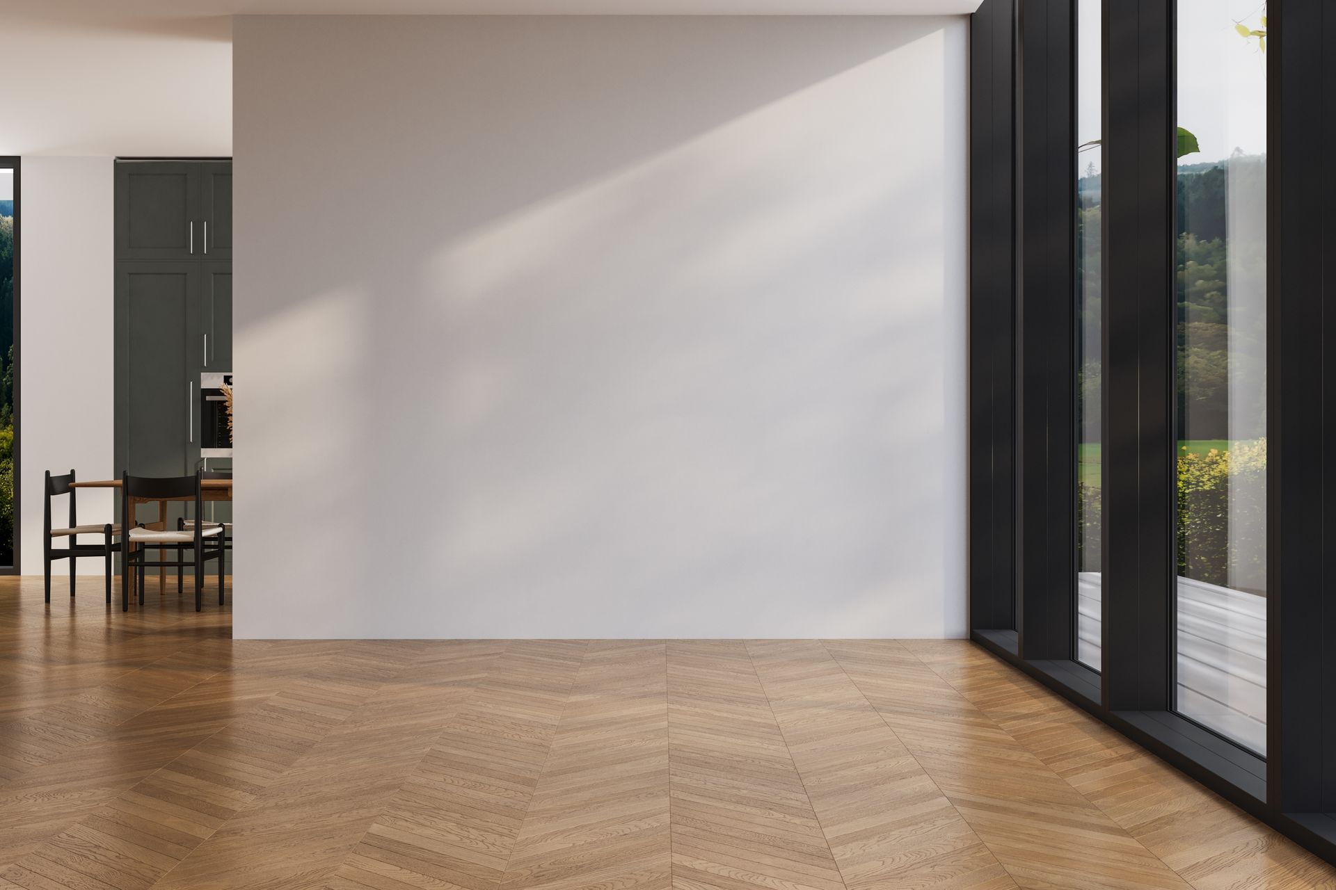 Empty room with white wall, wood floor, large windows, and a kitchen visible in the background.
