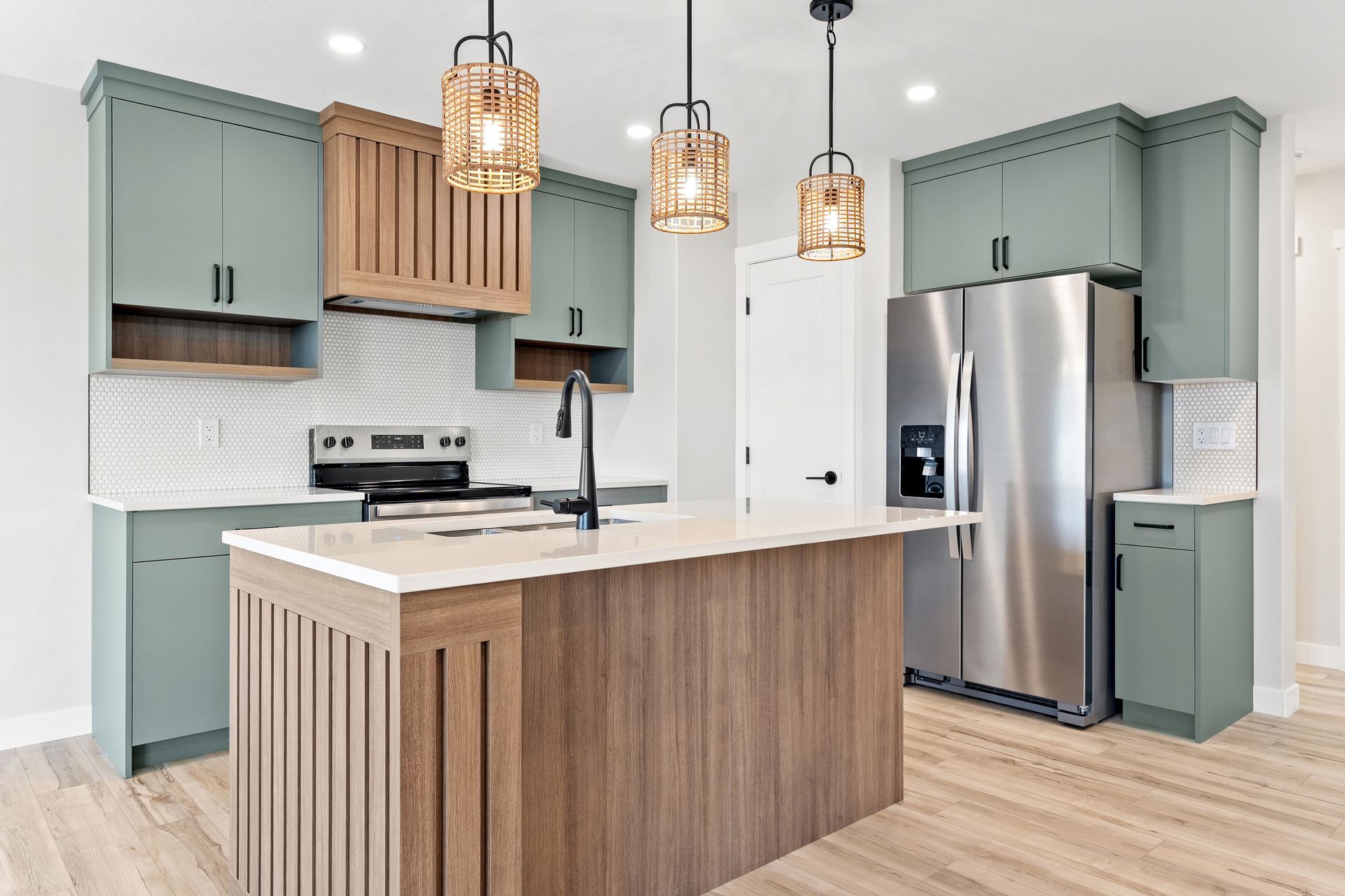 Modern kitchen with sage green cabinets, wooden island, and stainless steel appliances.