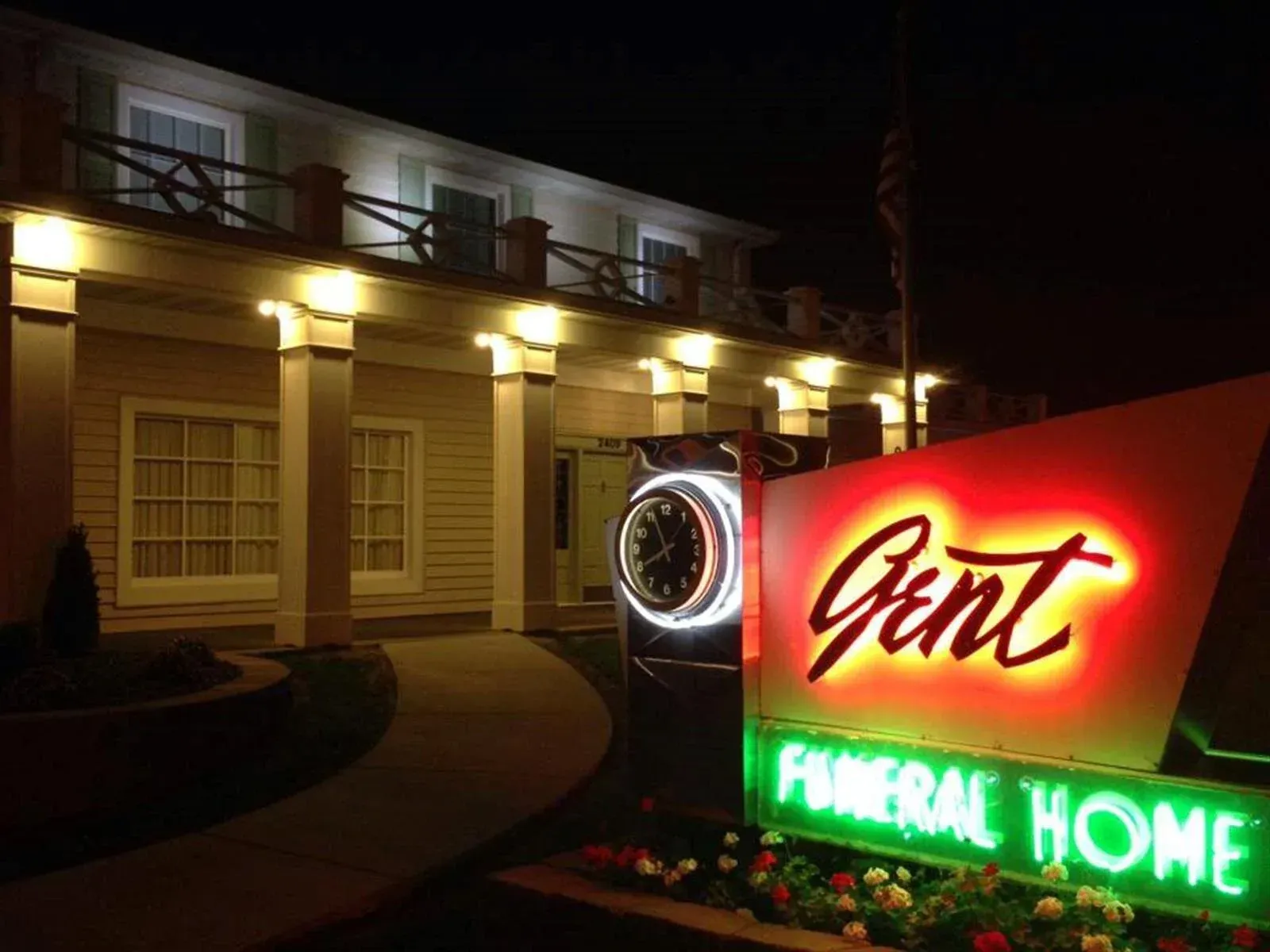 Nighttime exterior of a building with a glowing “Grint” sign and lit “Funeral Home” marquee