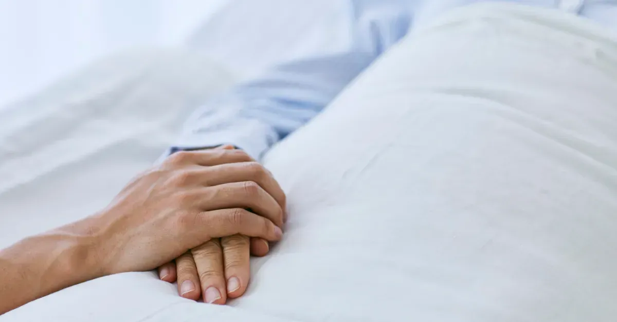 Hands clasped together on a white bed, suggesting comfort or support