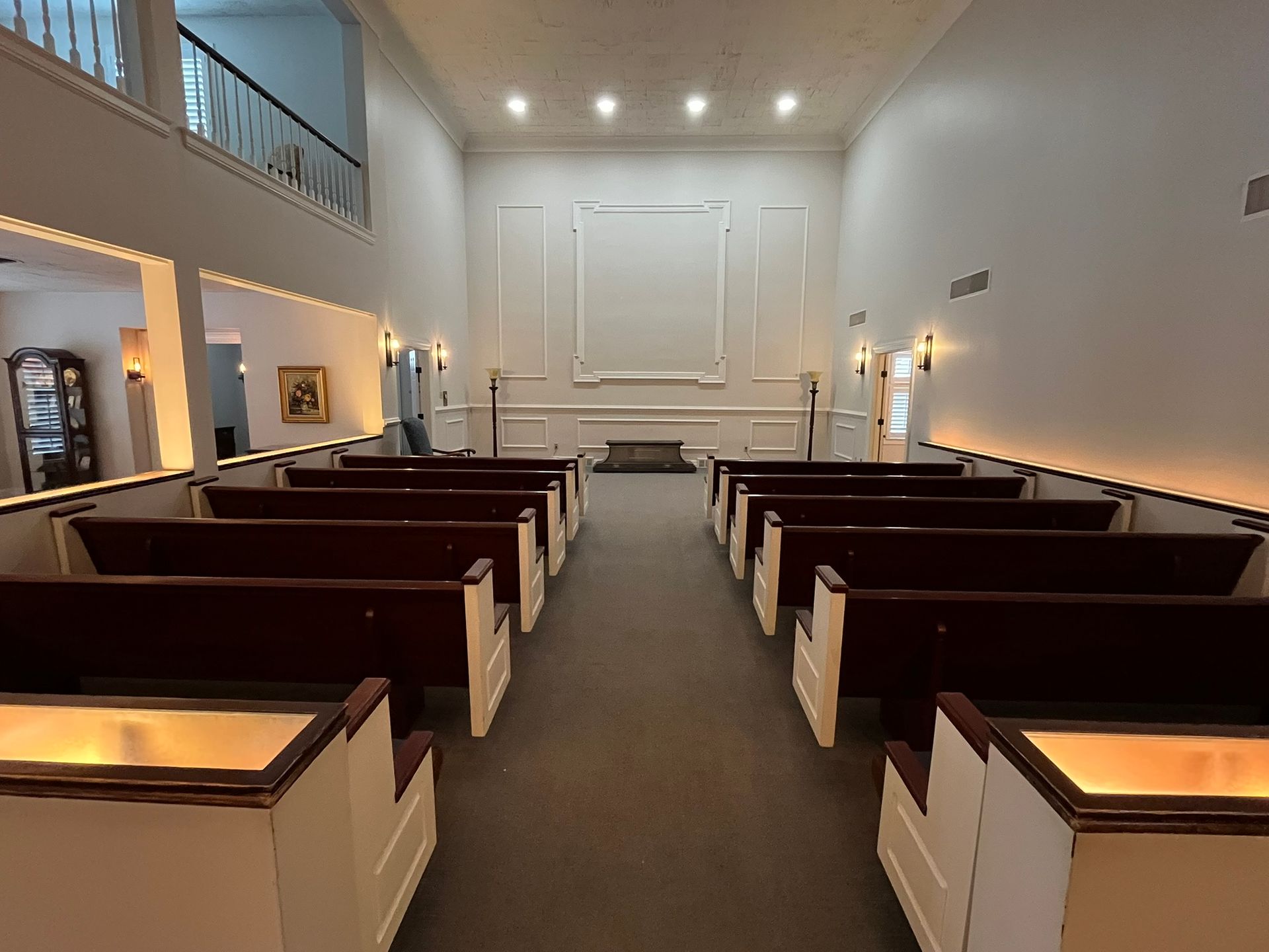 Empty church sanctuary with wooden pews, white walls, and warm recessed lighting viewed from the back aisle