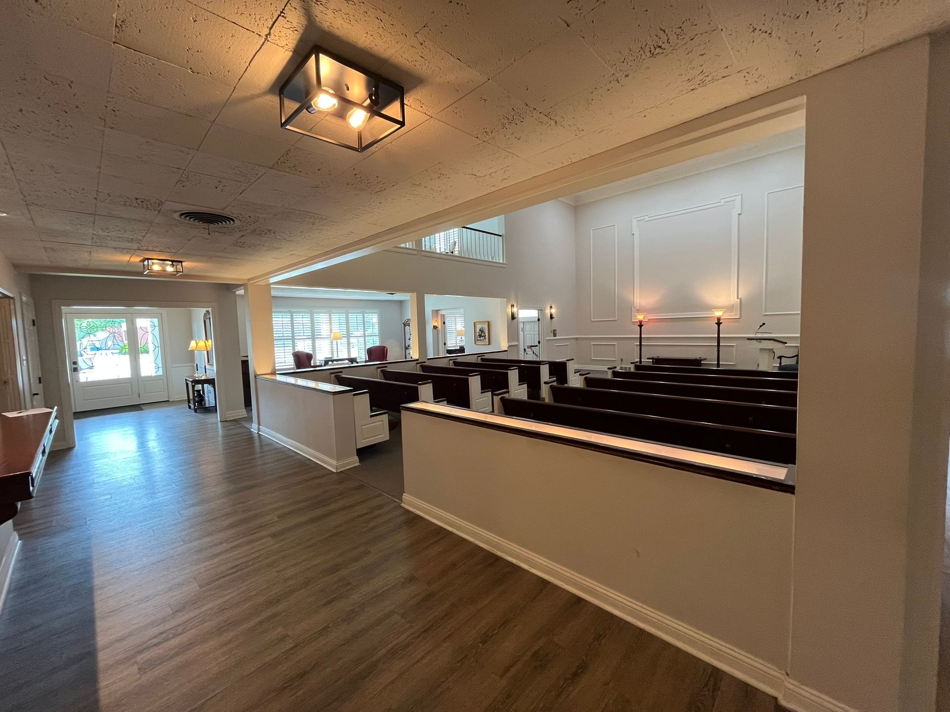 Bright church interior with pews, wood floors, and a white altar area under hanging lights
