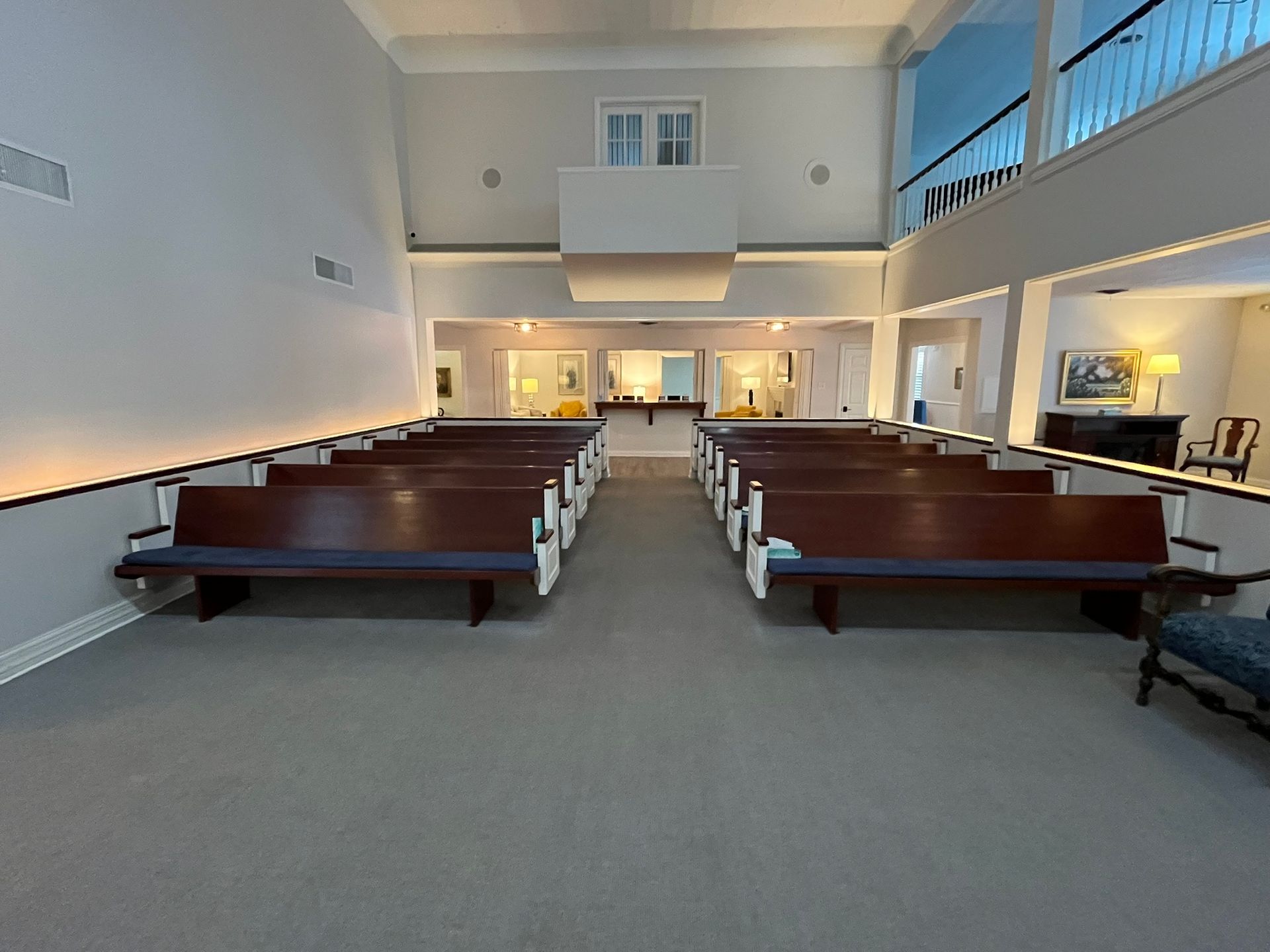 Empty church sanctuary with wooden pews, carpeted aisles, and a raised front altar area.