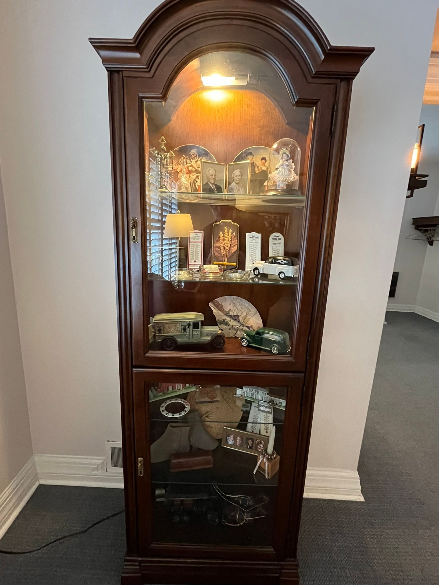 Dark wooden curio cabinet with glass doors, lit inside and displaying small decorative items.