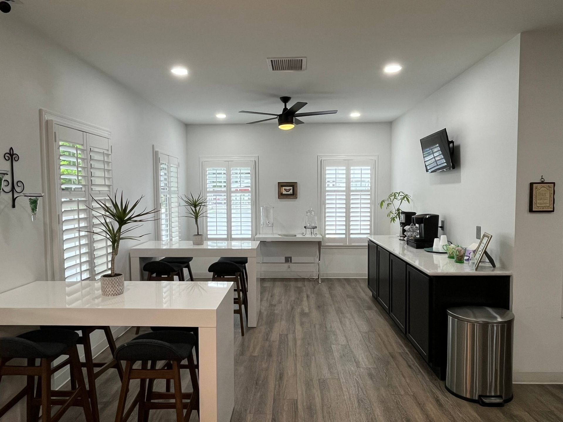 Bright modern kitchen with white island, black cabinets, wood floors, and large windows causing the room to be bright.
