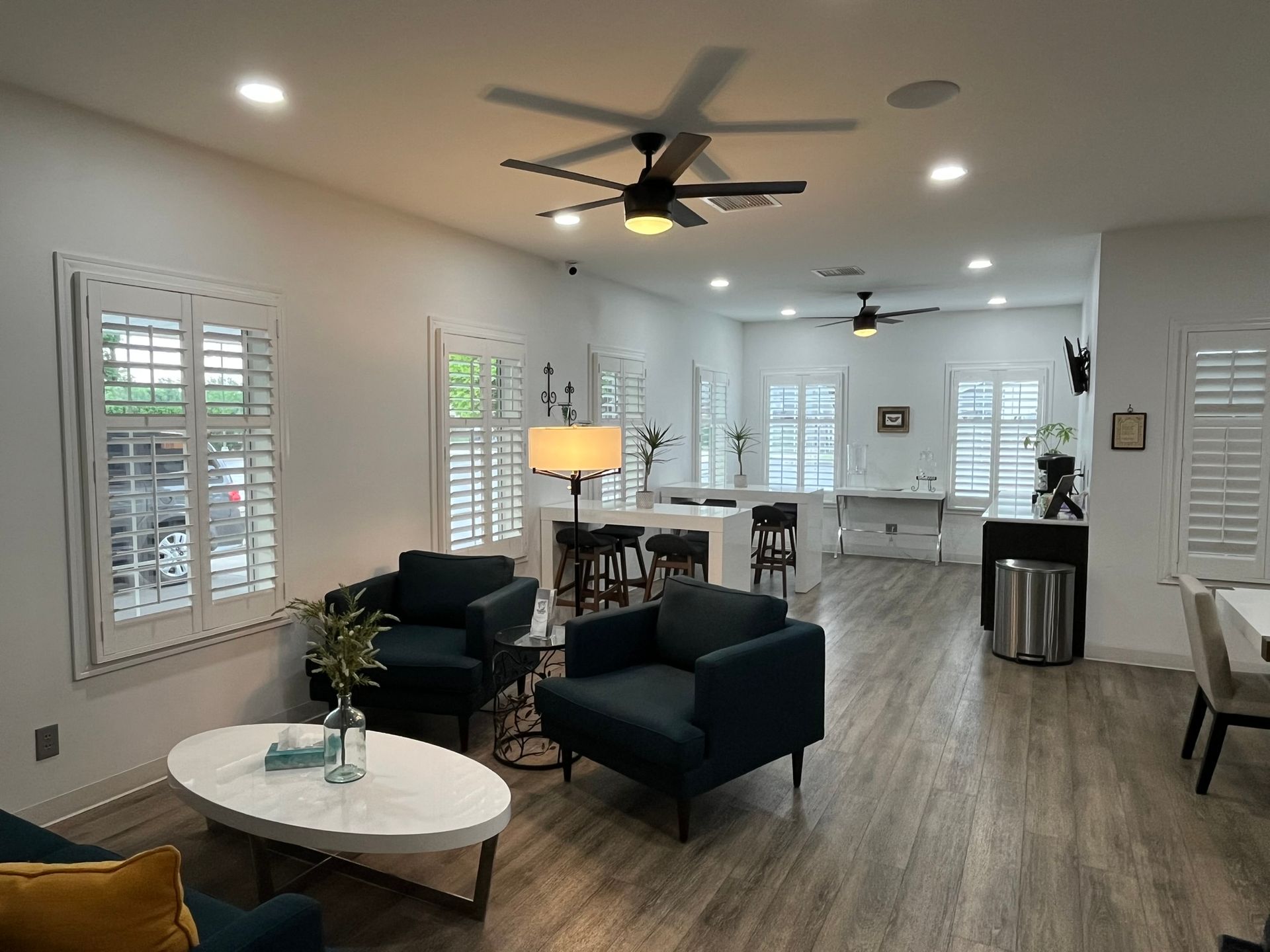 Bright living room with white walls, dark chairs, coffee table, ceiling fan, and dining area beyond