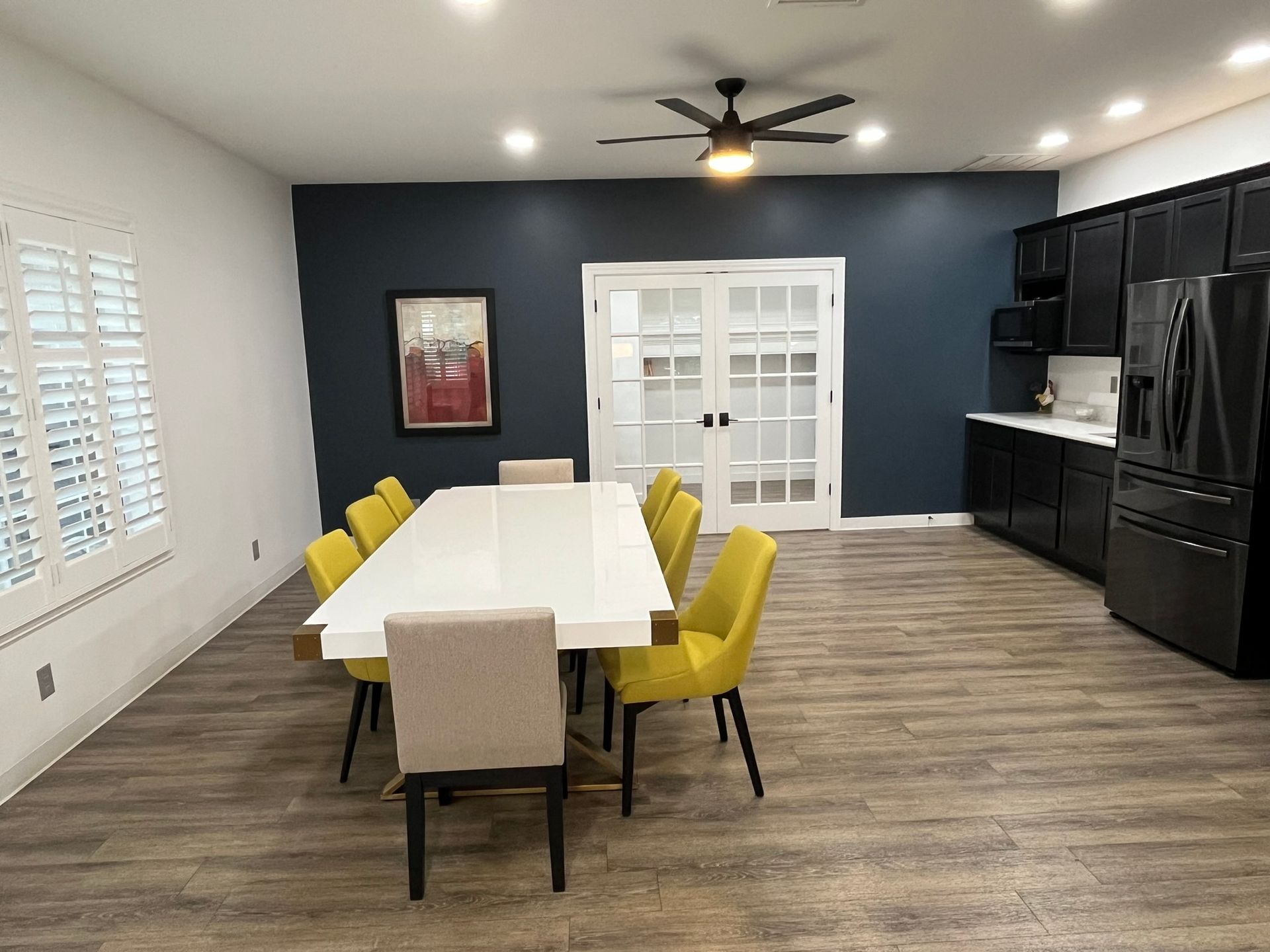 Modern dining room with white table, yellow chairs, dark cabinets, and large windows.