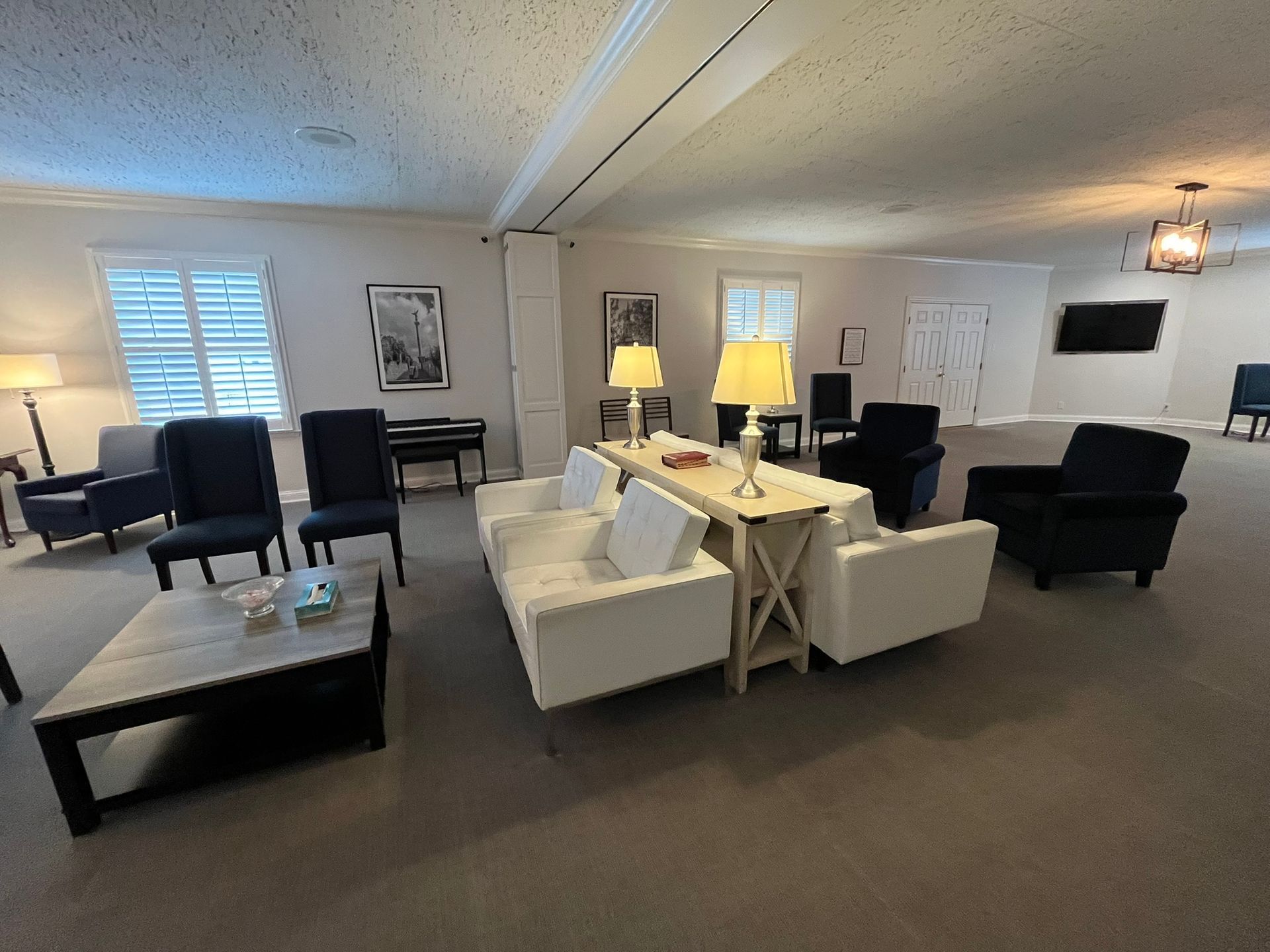 Large furnished living room with two white sofas, dark chairs, lamps, and a wall-mounted TV