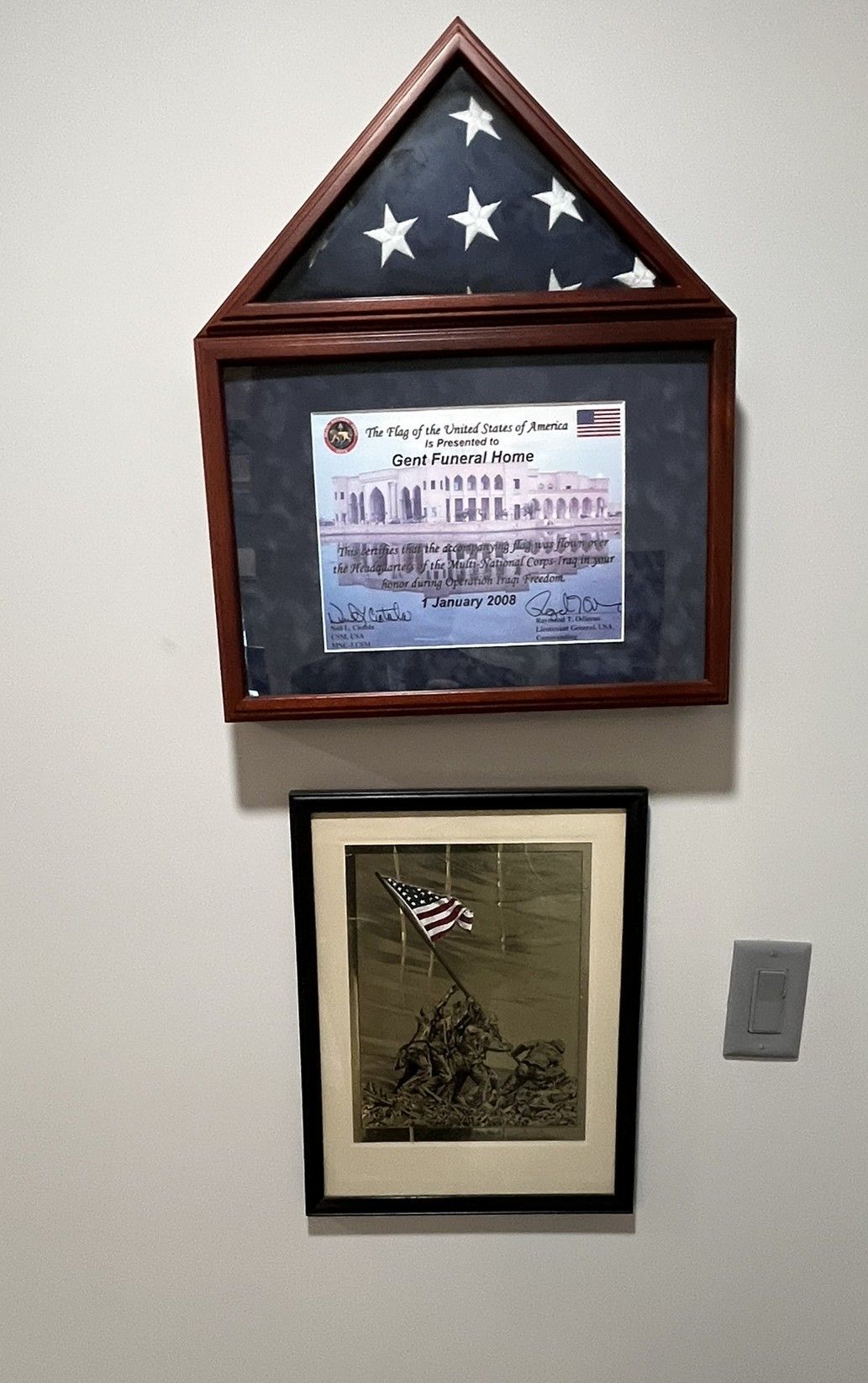 Framed military memorial display with folded American flag, certificate, and portrait on a wall