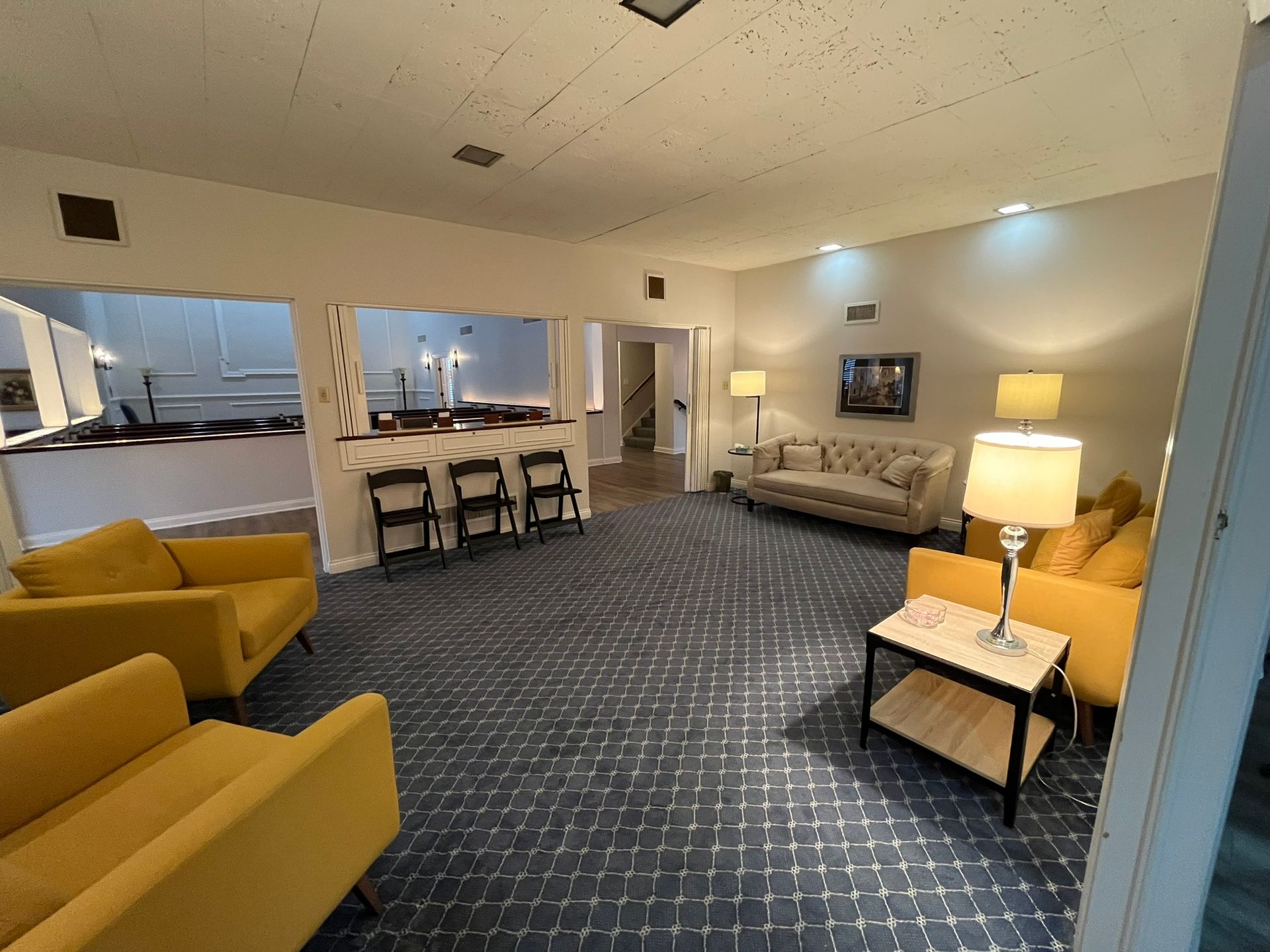 Modern lounge with mustard chairs, sofa, floor lamps, and a small table beside a checkered carpet.