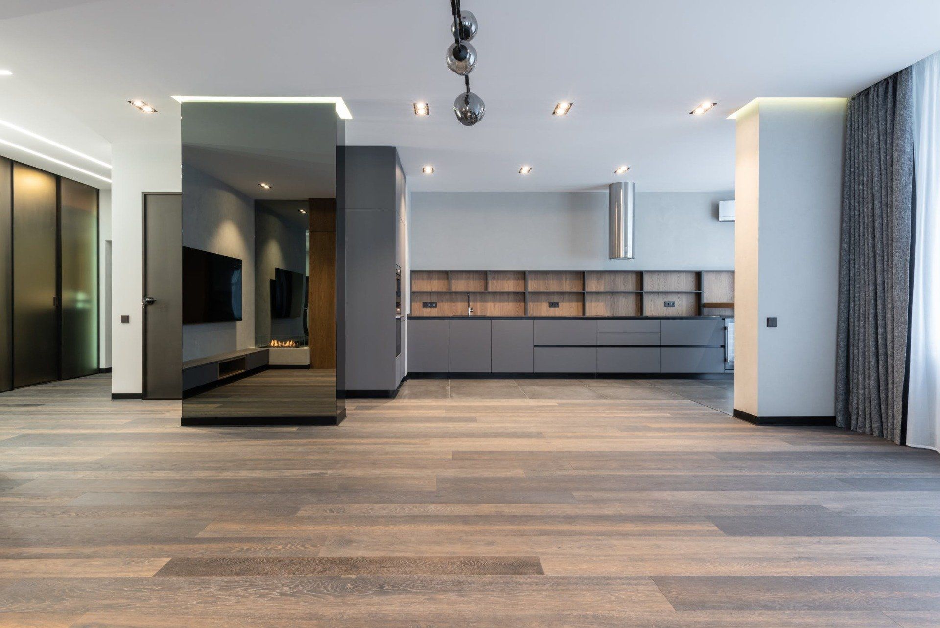 Modern, minimalist kitchen with gray cabinets, a large mirror, and wood flooring.