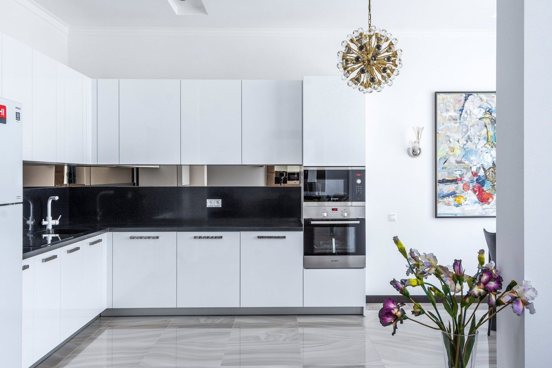 Modern white kitchen with black countertops, stainless steel appliances, and colorful abstract art.
