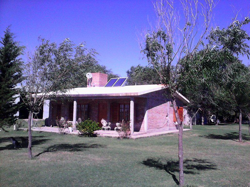 Pequeña casa de ladrillo con porche, césped verde, árboles y cielo azul.