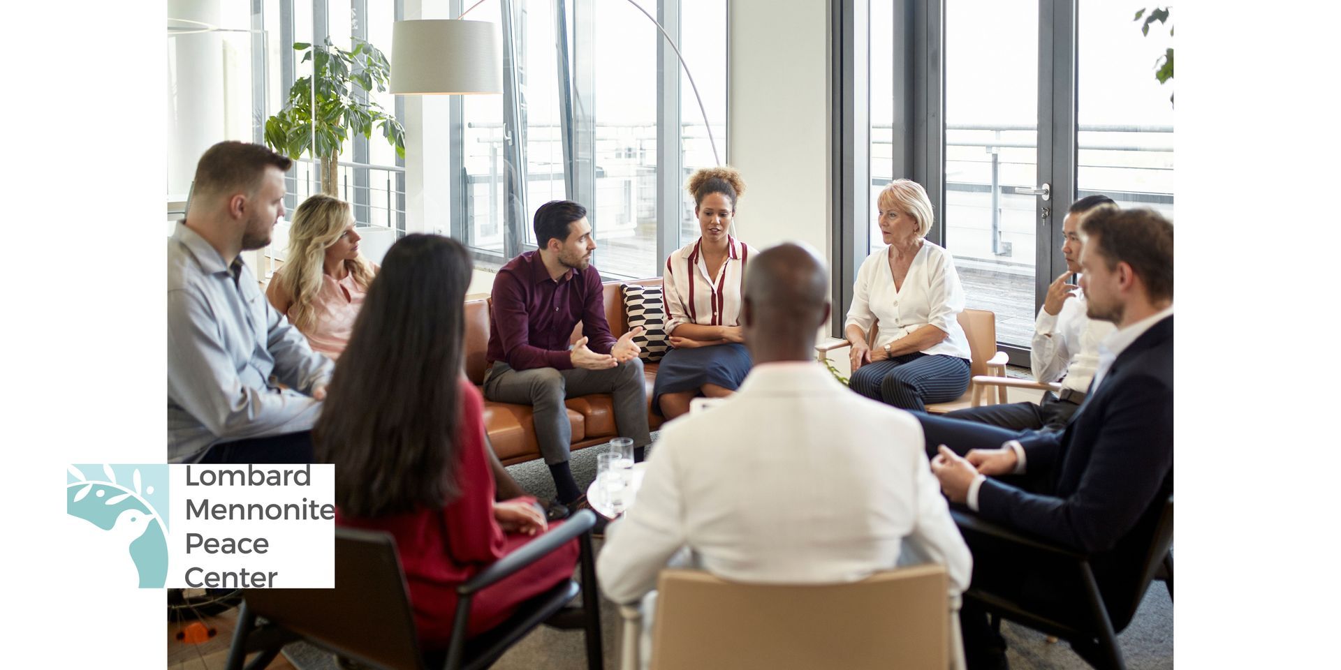 Group of 9 people seated in conversational group around a coffee table in a daylight-filled space, talking and listening to each other.