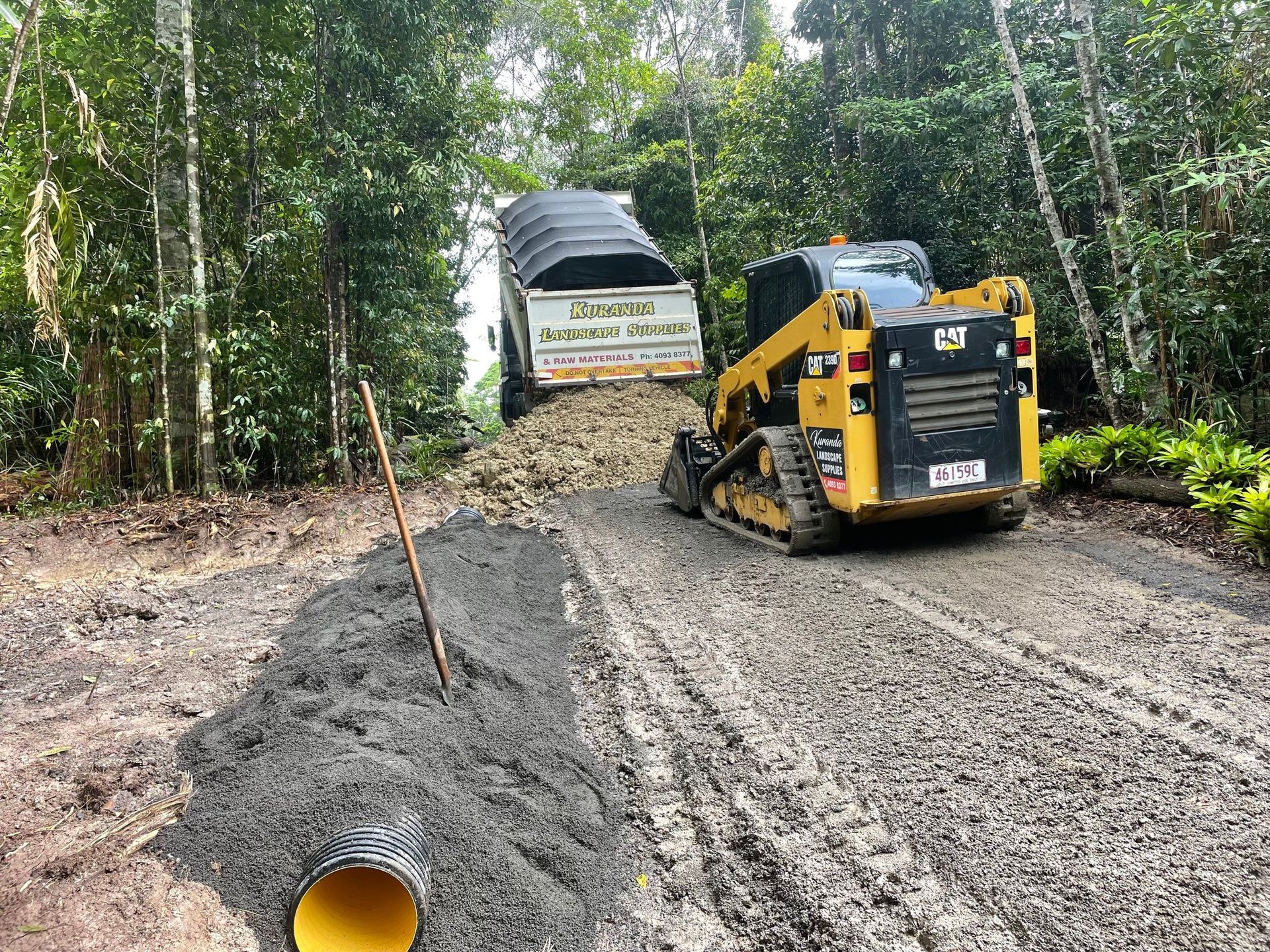 A skid steer loader and truck are working on a dirt road in a forest — Kuranda Landscape Supplies in Kuranda, QLD