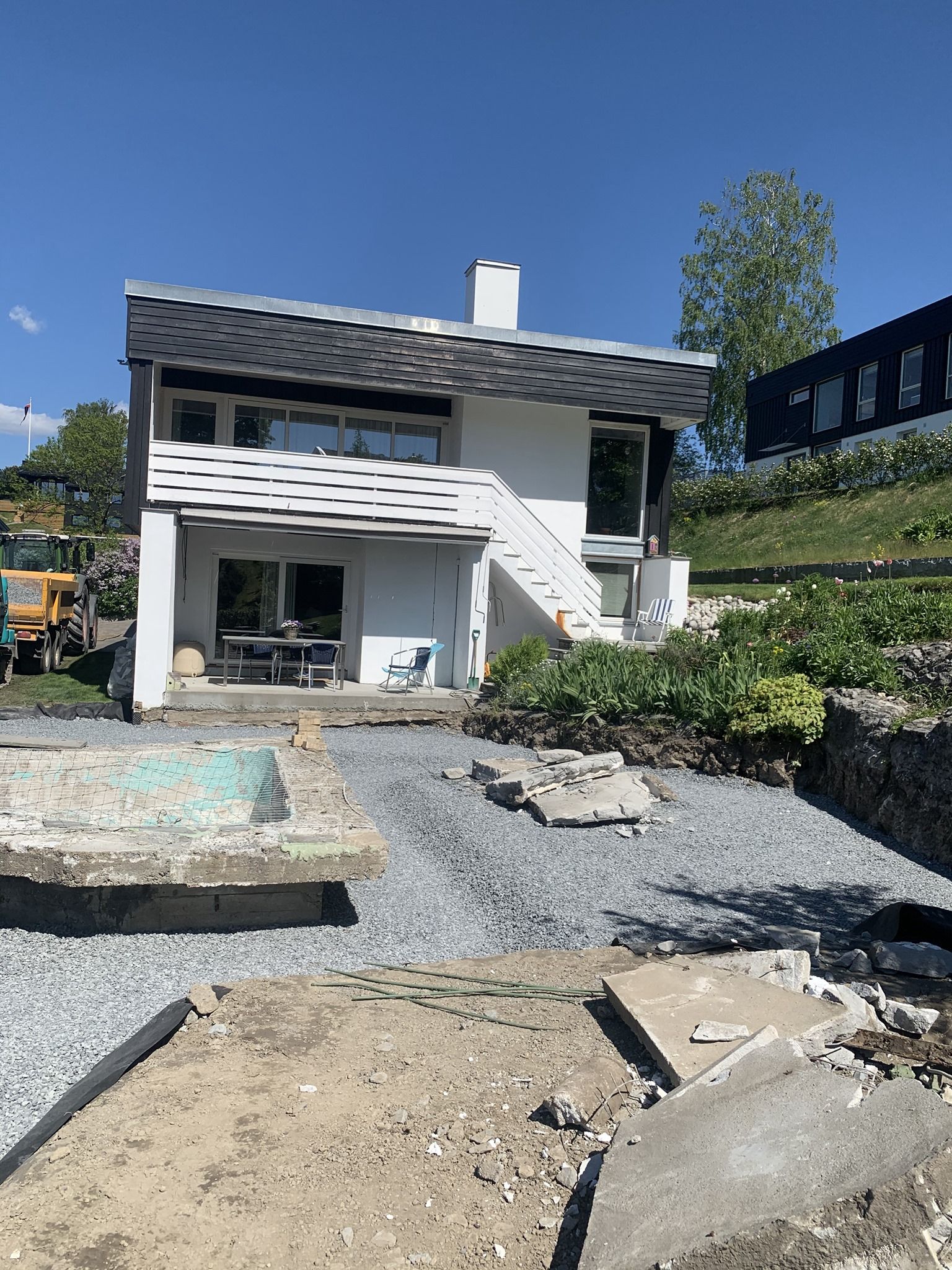 Moderne hvitt hus med uteplass, grusgård og hage under en klar blå himmel