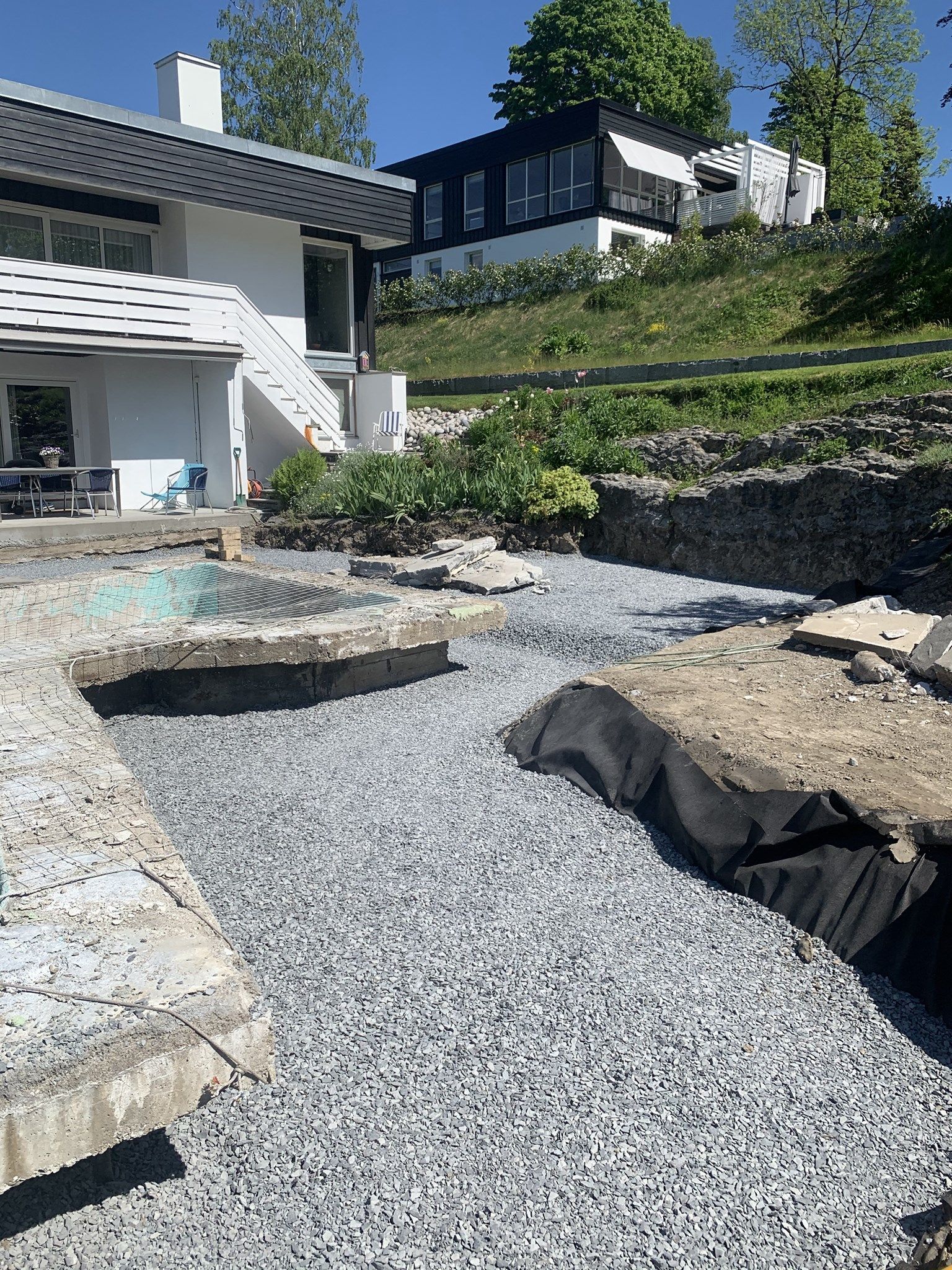 Gruskledd bakgård med steintrapper, terrassert støttemur og moderne hus på en solrik dag