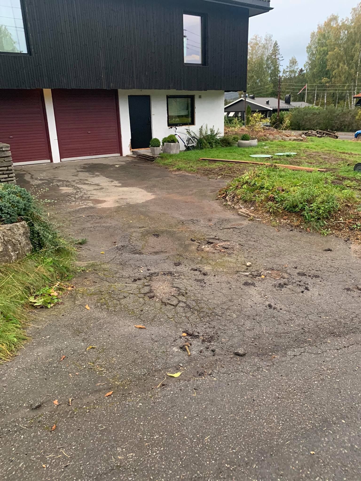 Innkjørsel og forside av et hus med en rød garasjeport, hvit undervegg og en grusgård.