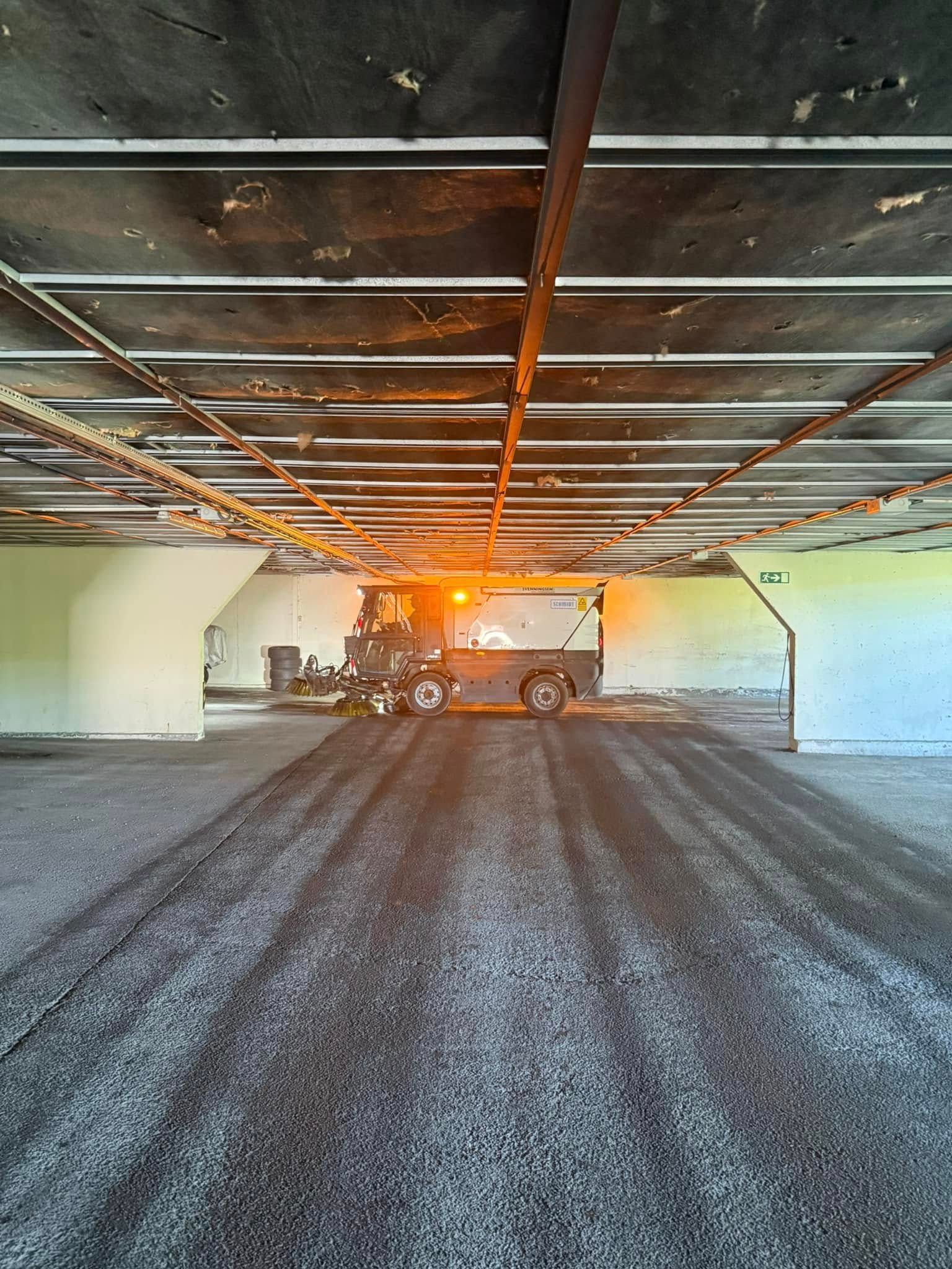 Sølvfarget semitrailer med blå containere parkert på en grusplass, med en haug med treavfall.
