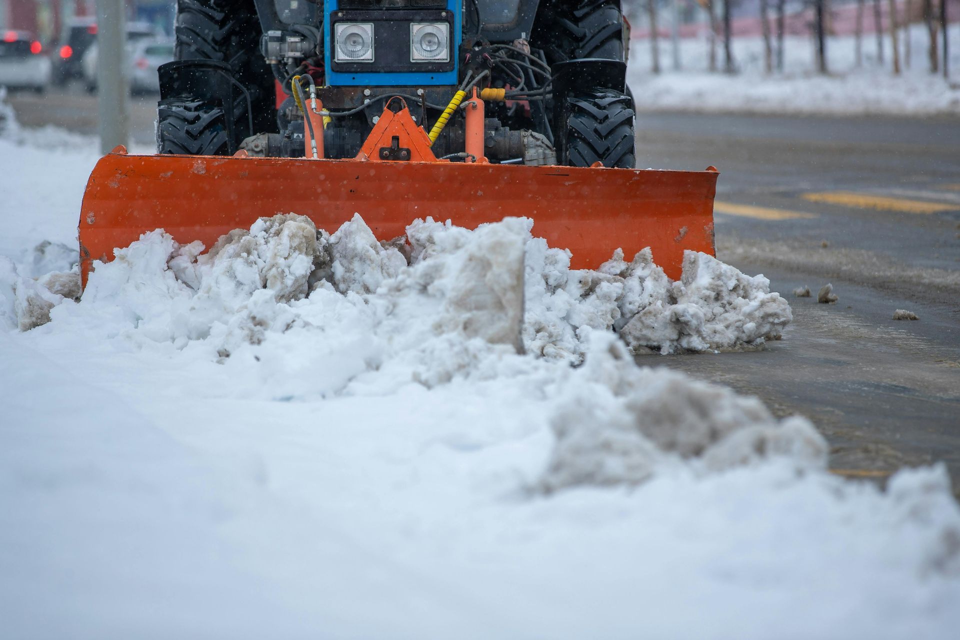 Oransje snøplog skyver snø langs en våt gate