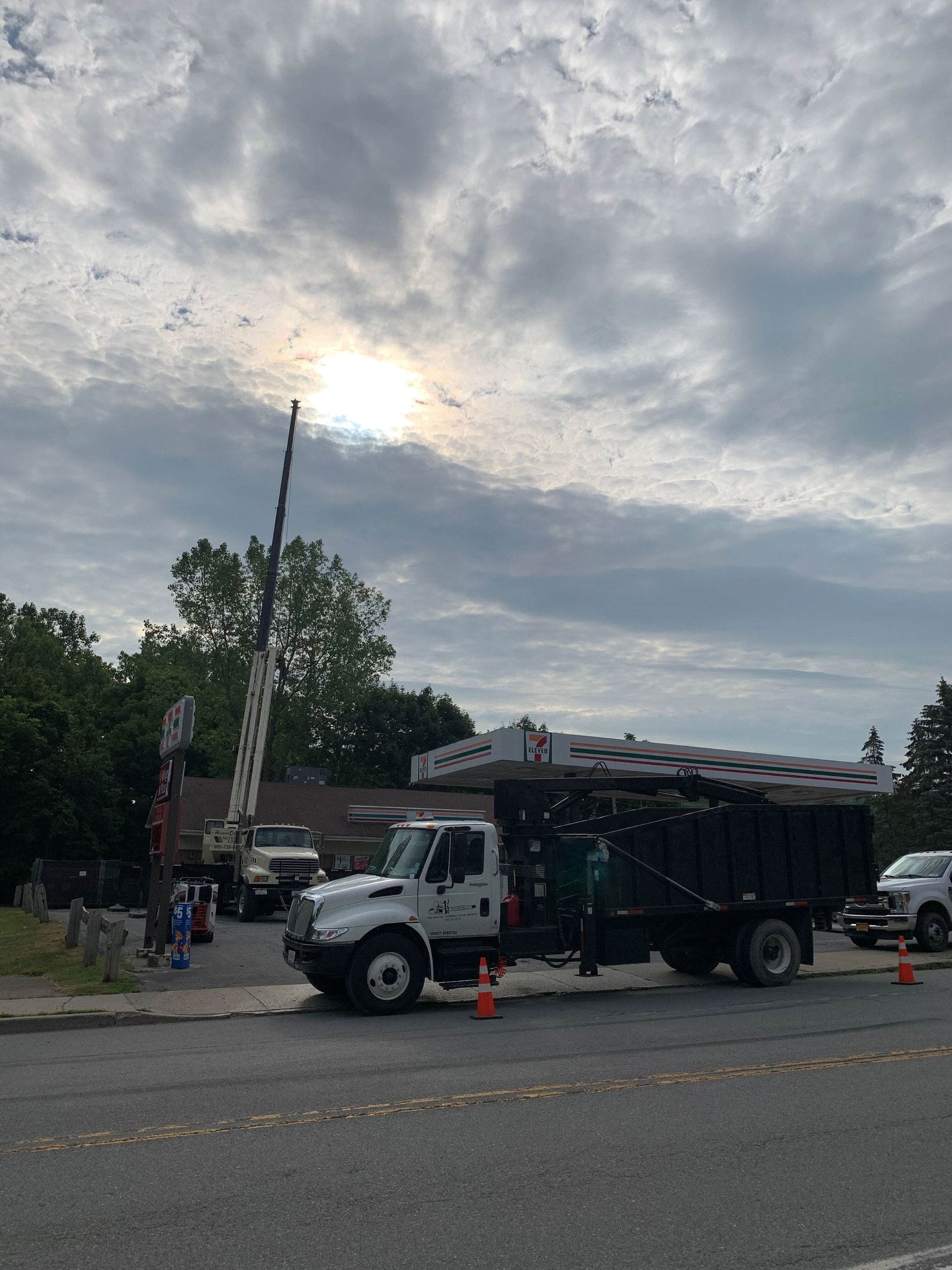 A white construction truck with a flatbed load parked on a street near a crane under a cloudy sky.
