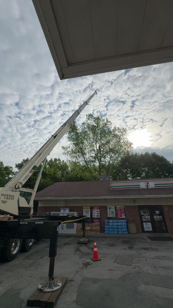 A utility truck with an extended crane parked in a brick building's parking lot under a cloudy, sunny sky.