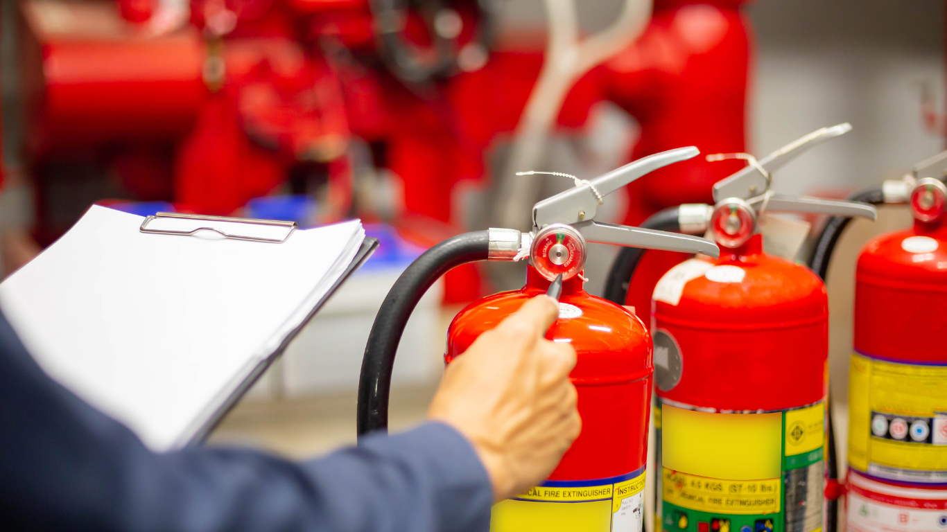 A person holds a clipboard while inspecting red fire extinguishers in a professional setting.