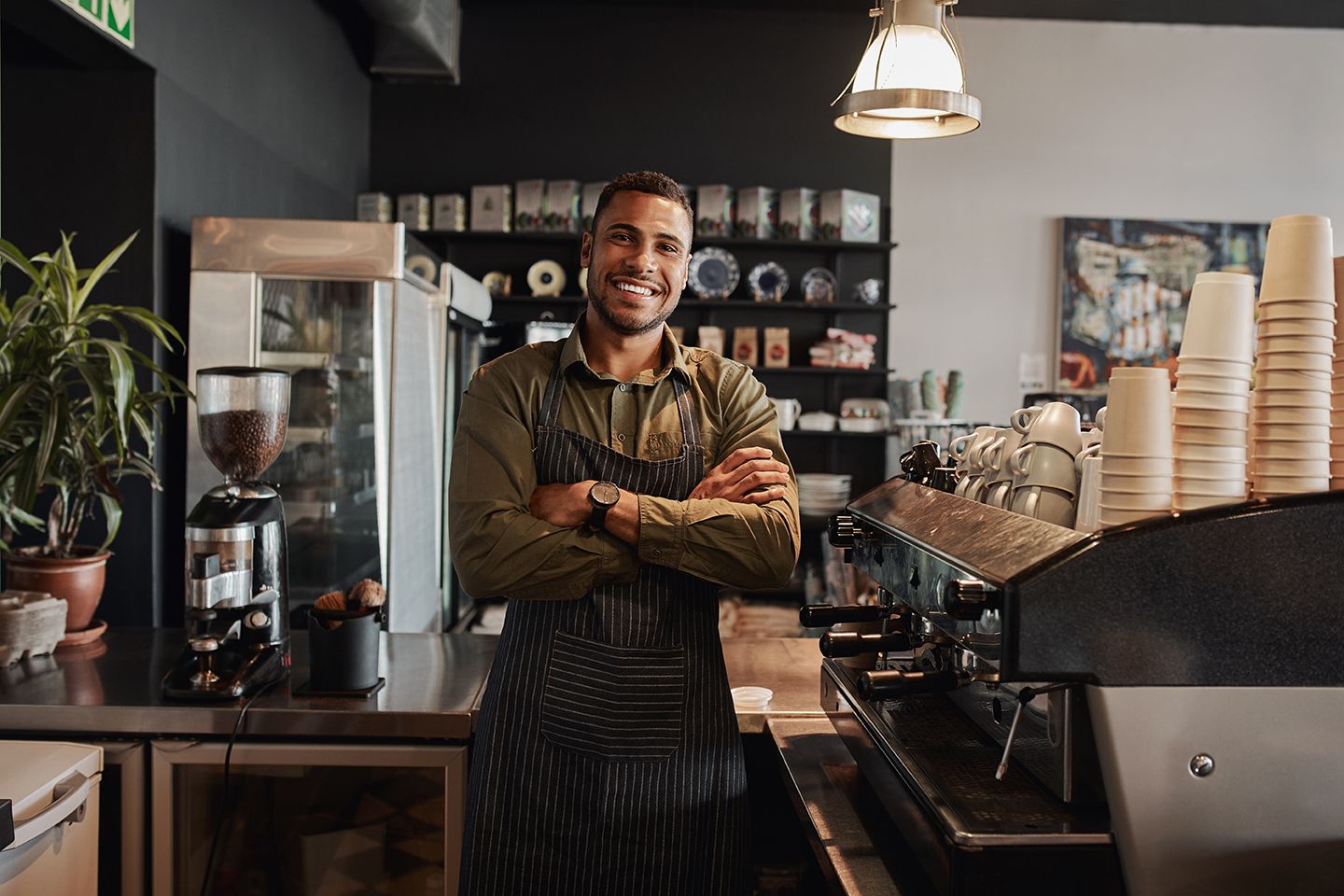 A man is standing in a coffee shop with his arms crossed.